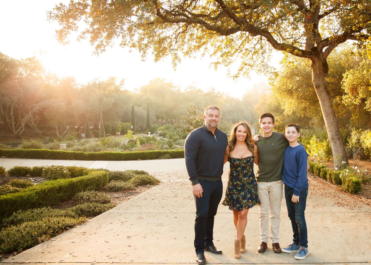 Family group portrait session at golden hour under autumn trees on a winding path.