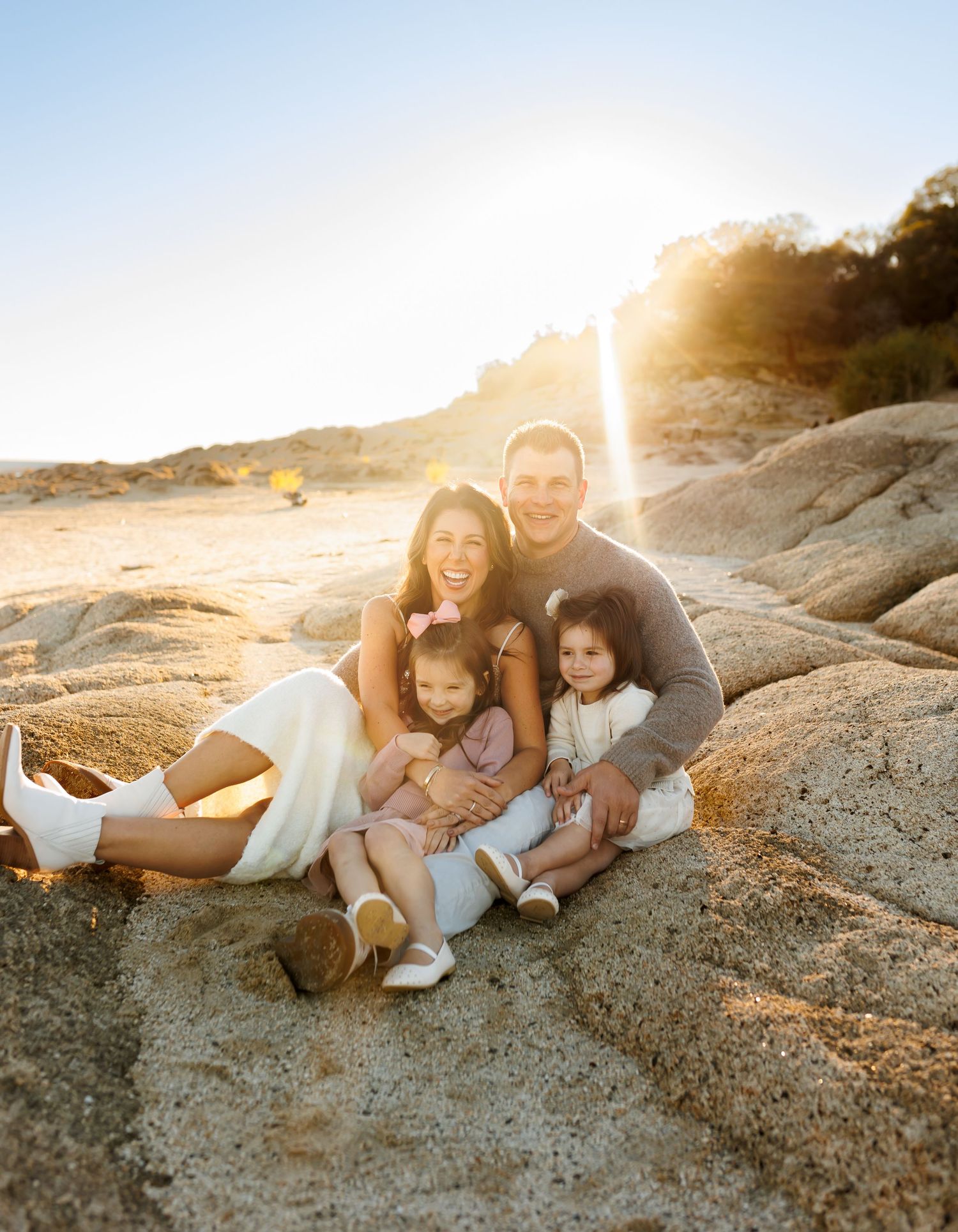 Family enjoying a sunset moment together while sitting on rocky coastal terrain during a warm golden hour.