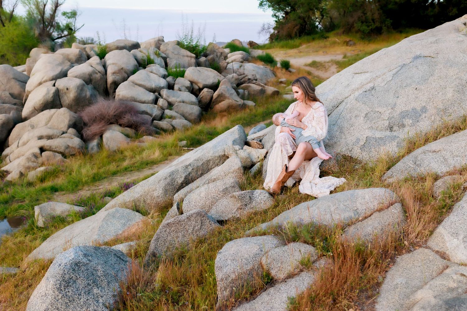 Young woman sitting on large granite rocks near the coast, surrounded by wildgrass and boulders at dusk.
