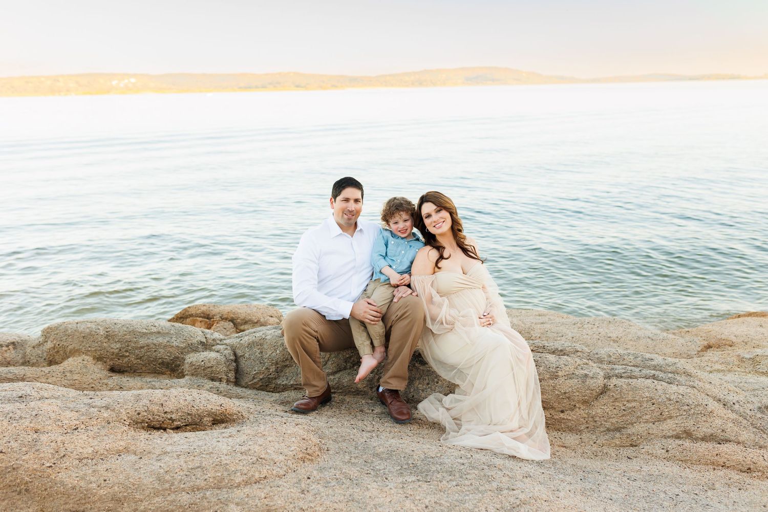 Coastal family photography session on rocky shore during sunset with ocean backdrop.