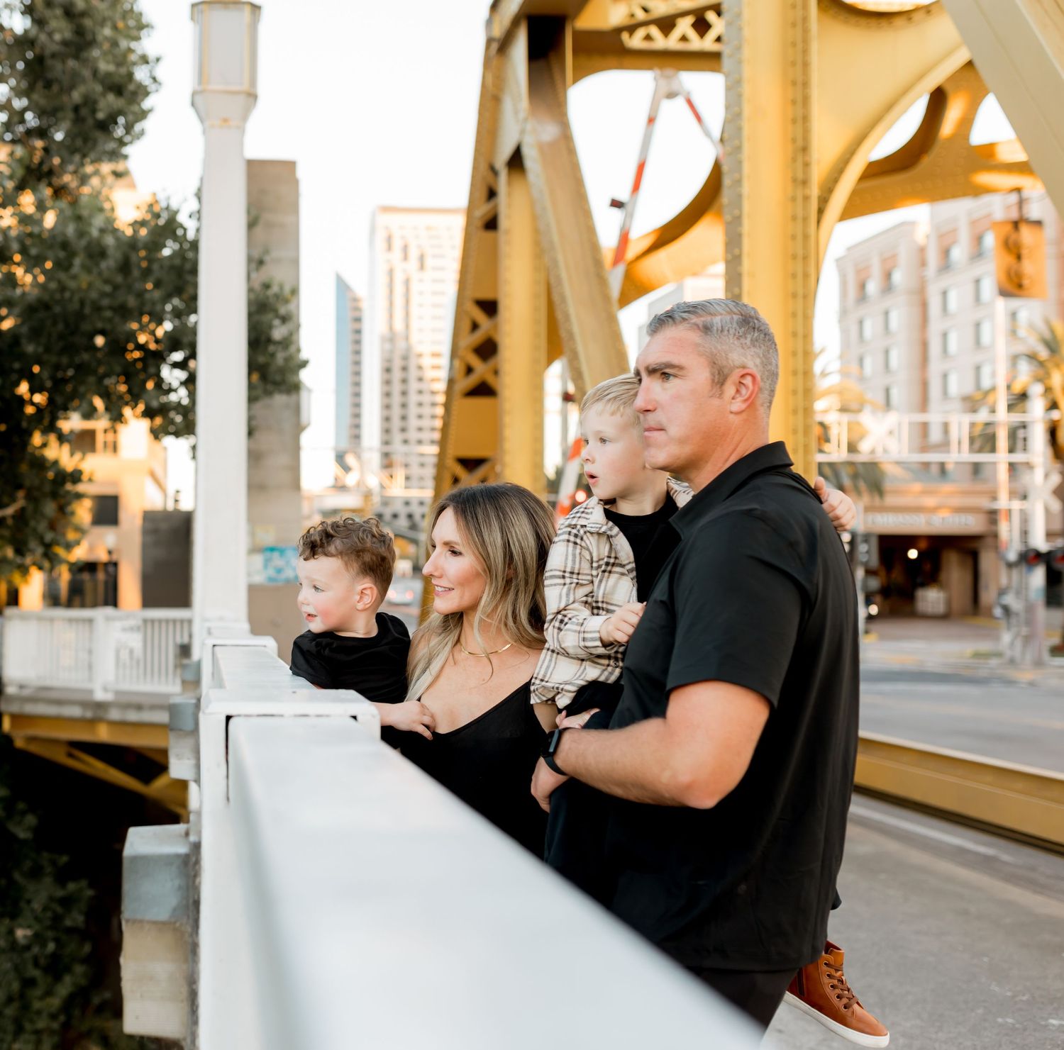 Family portrait session on yellow bridge with city buildings in background.