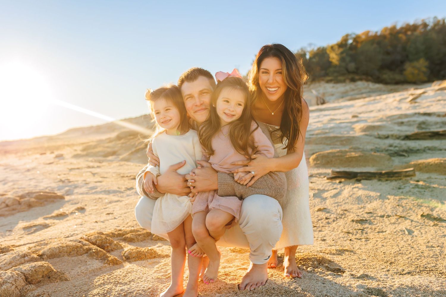Family sitting together on a rocky beach during golden hour with warm sunlight and coastal scenery.