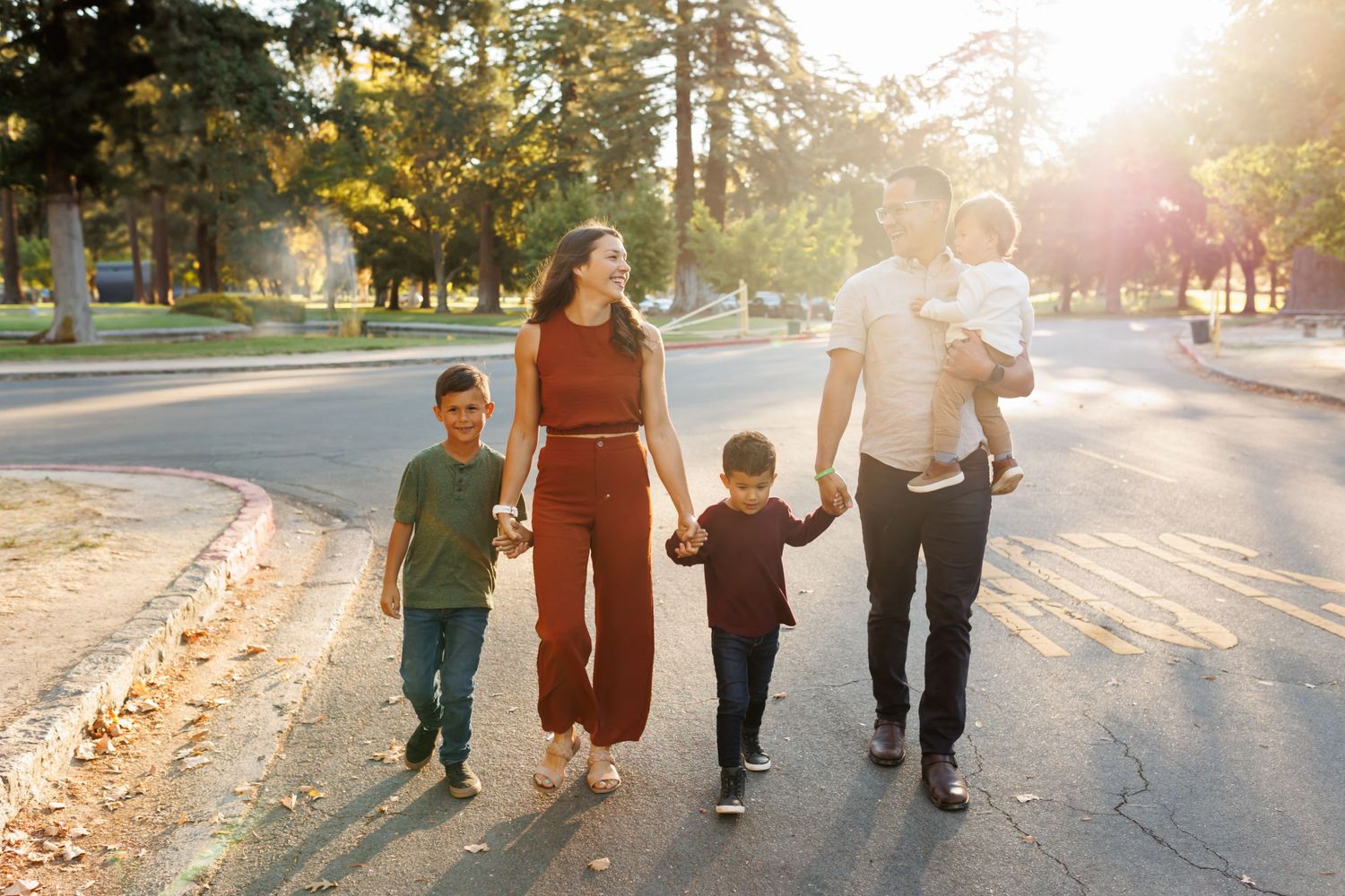 Silhouettes of a family walking together on a tree-lined path during sunset.