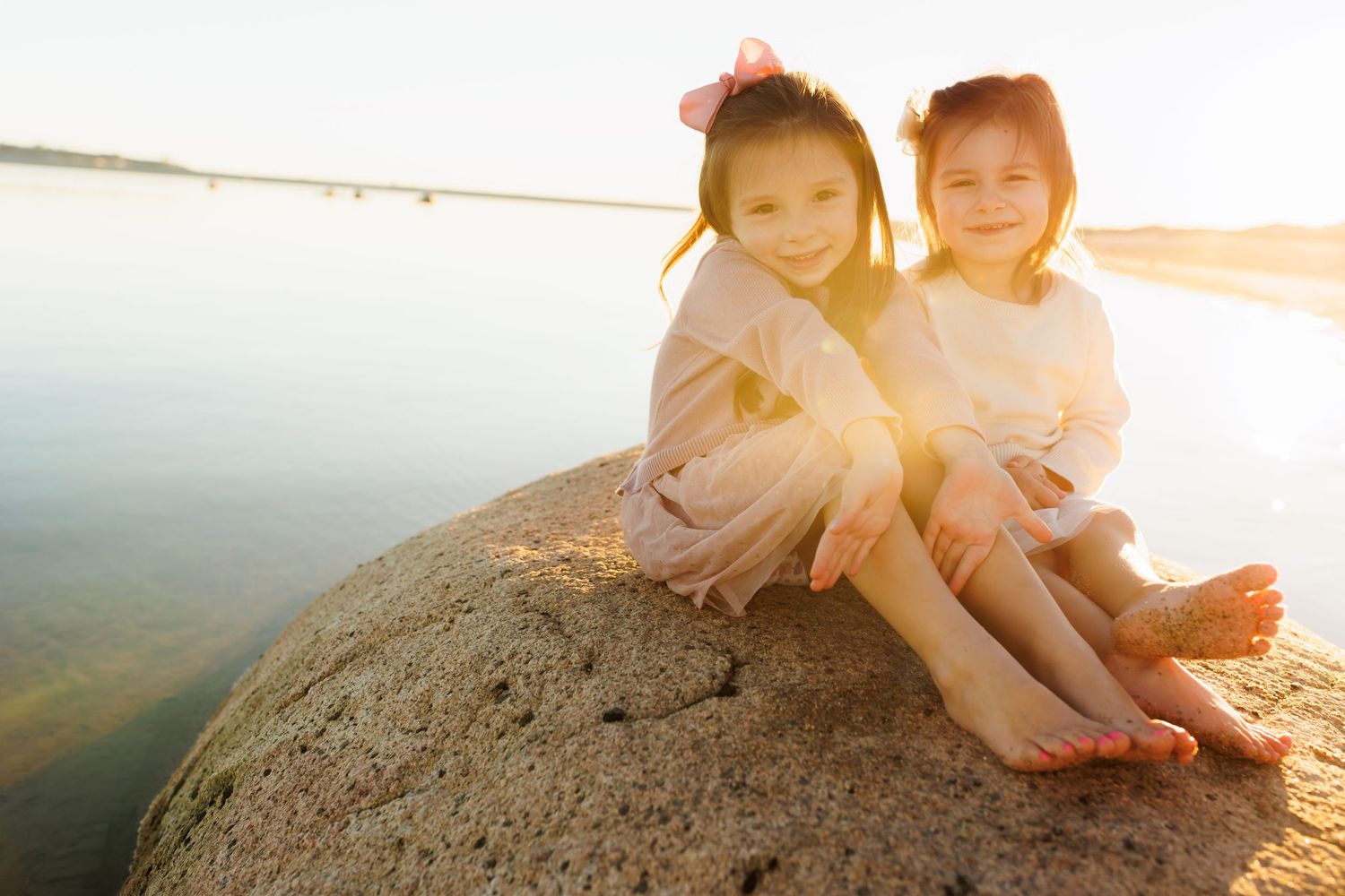 Couple sits together on sandy beach at sunset with soft glowing light.