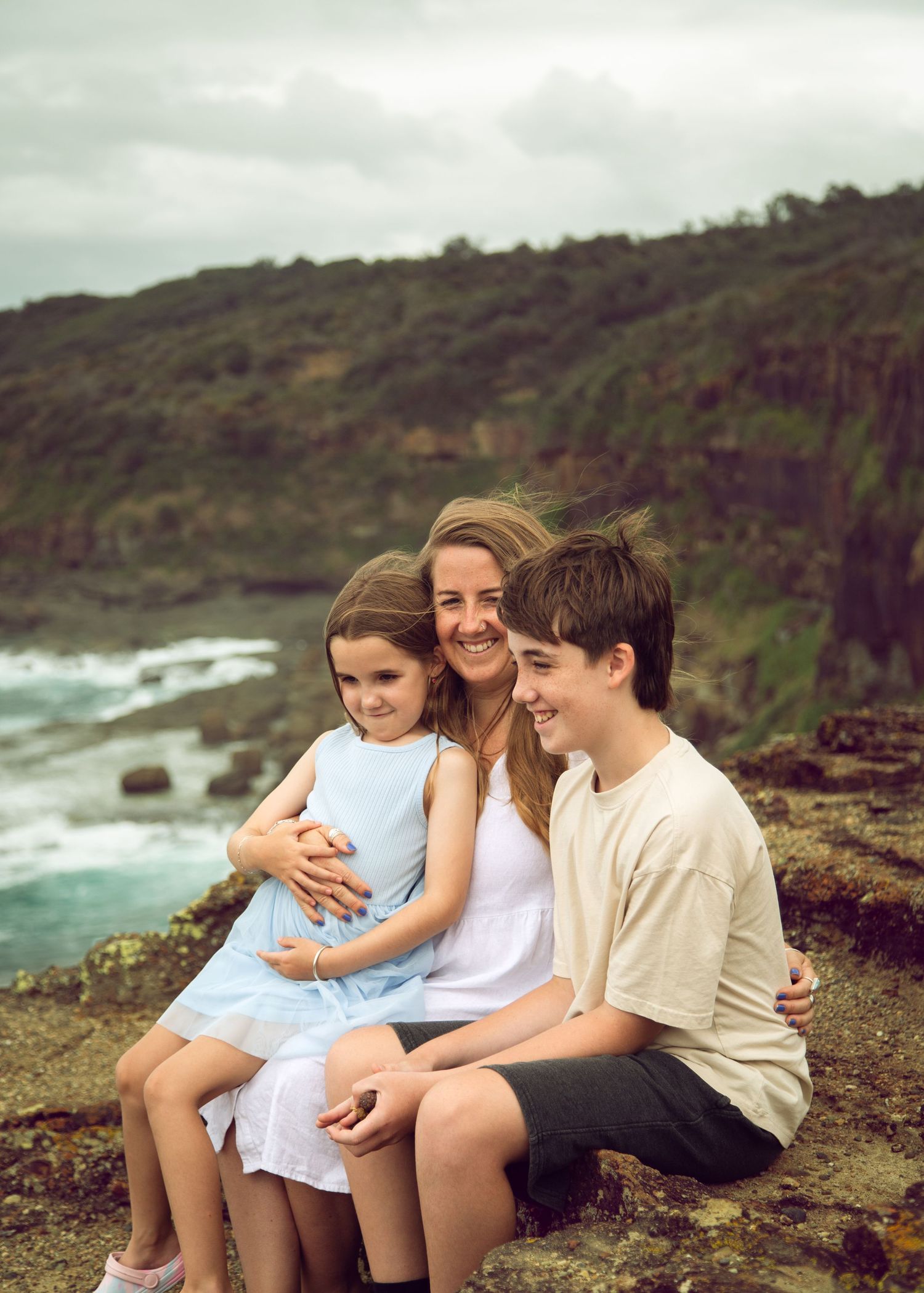 A mum and her two children on a cliff top. Smiling laughing faces.