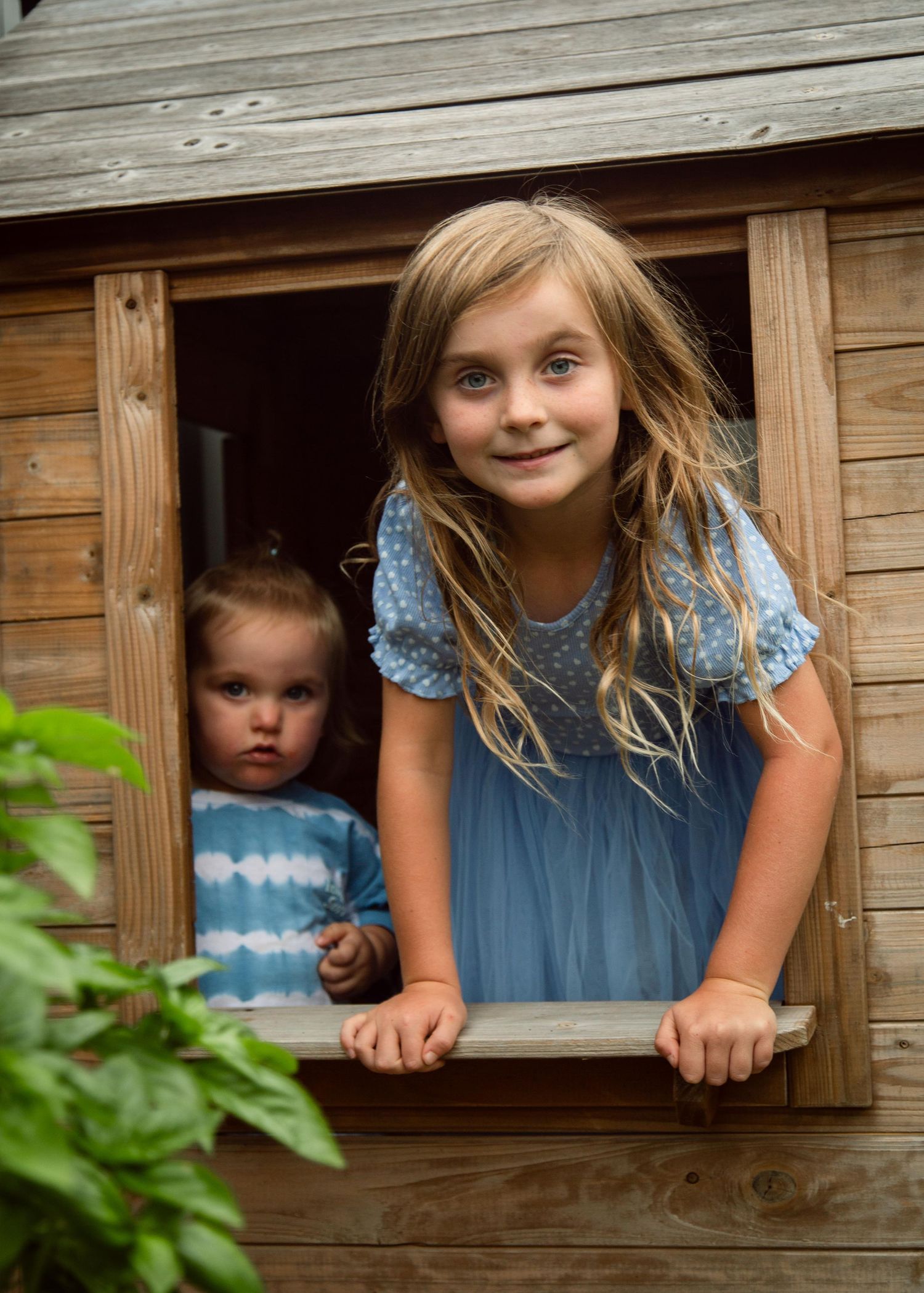 Two children looking out a window of a outside playhouse