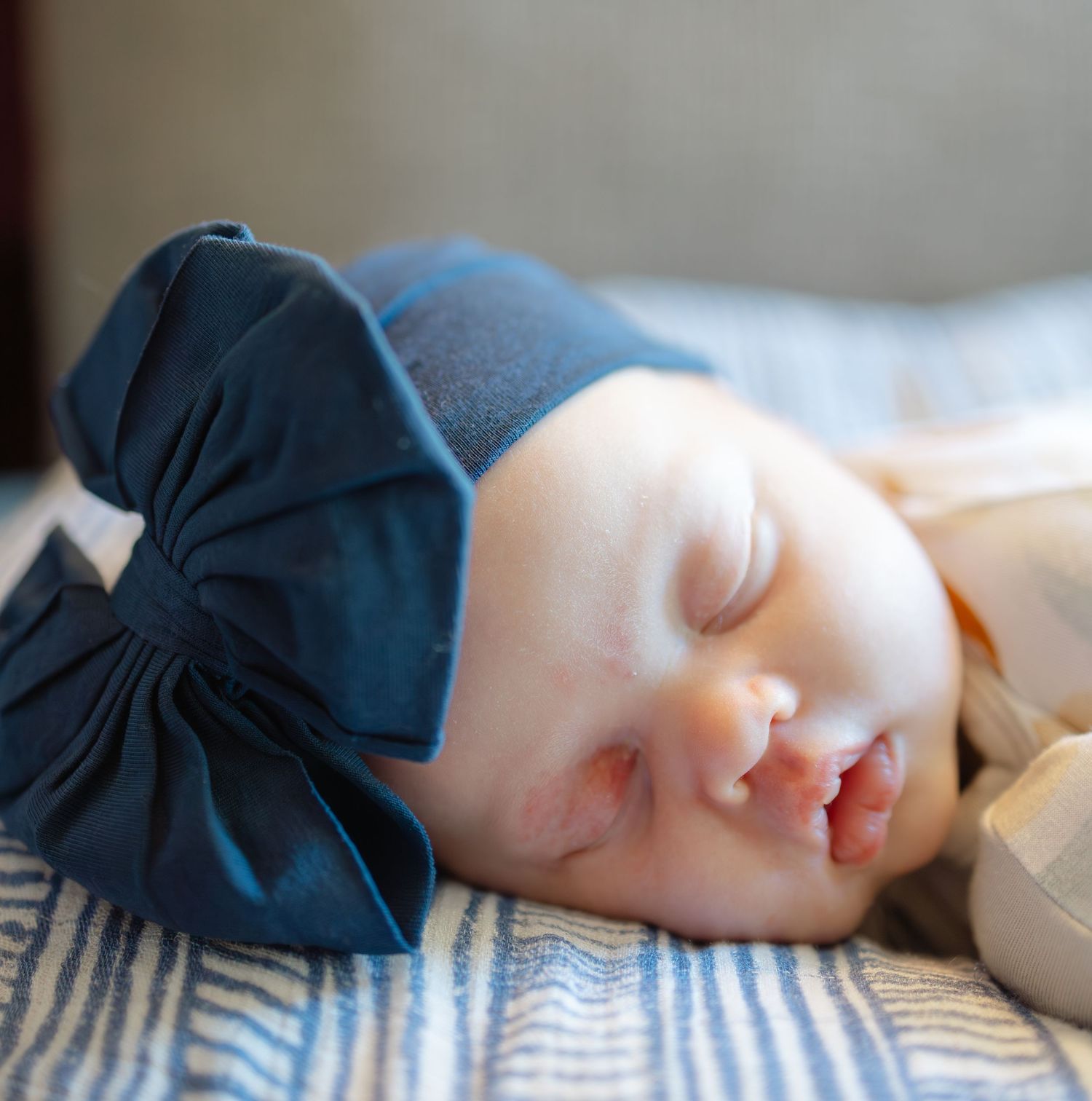 Sleeping newborn baby wearing a navy blue bow hat, resting peacefully on a striped blanket.