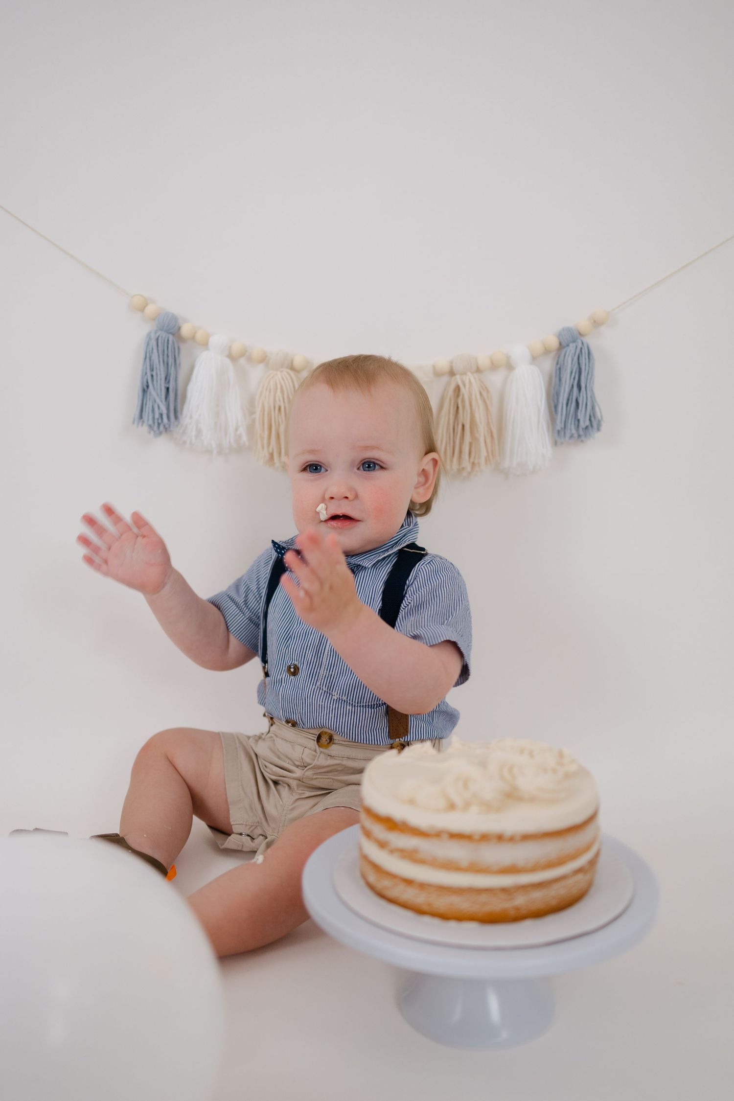 Sweet one year old celebration with smash cake setup featuring blue and cream tassel banner decor.