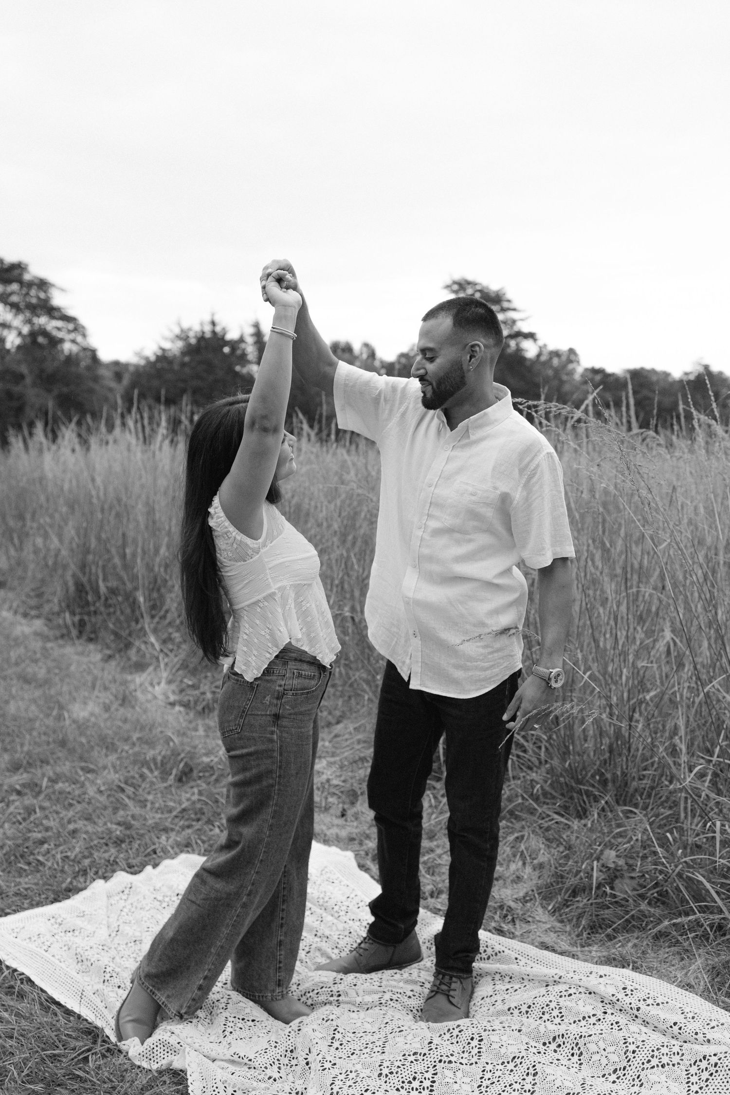 Black and white photo of a couple dancing outdoors in a field, man spinning woman on a blanket.