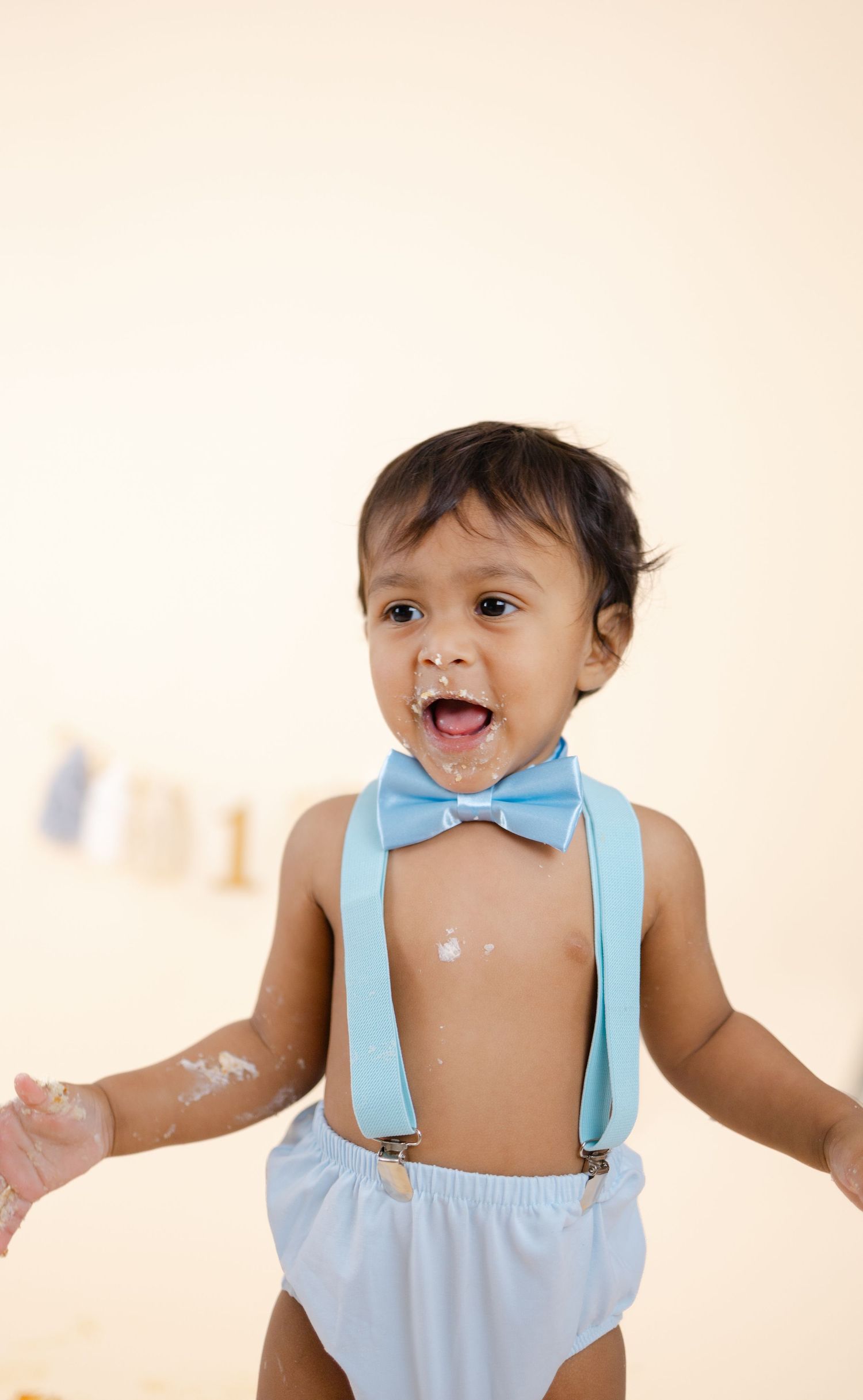 A toddler wearing a light blue outfit with suspenders and bow tie smiles and plays in a series of connected photos.