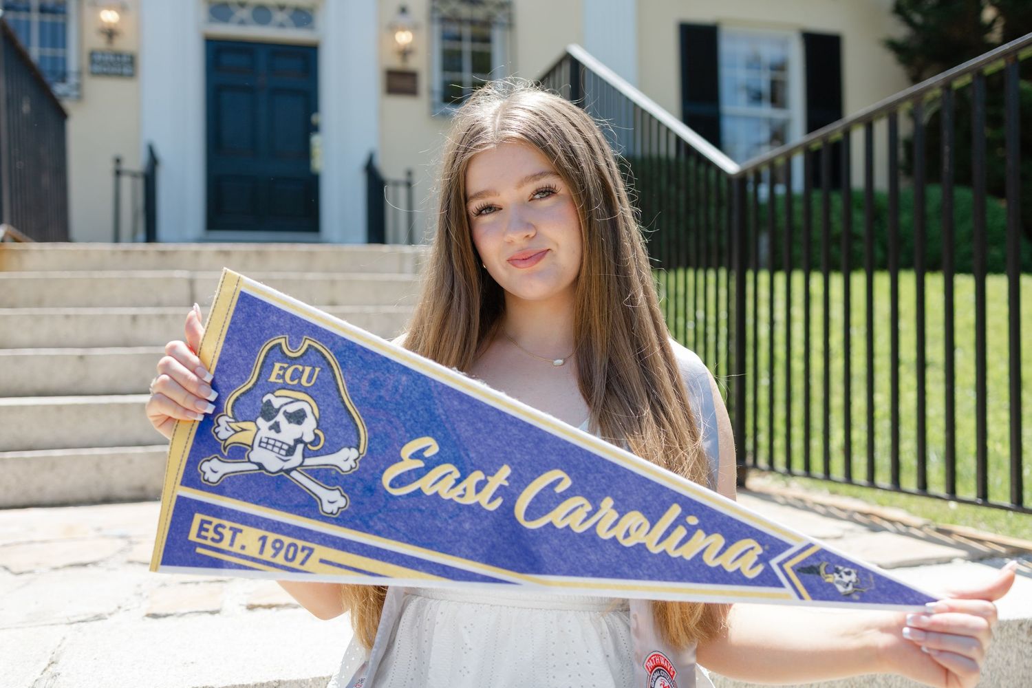 Student displays East Carolina University pennant in front of campus building.