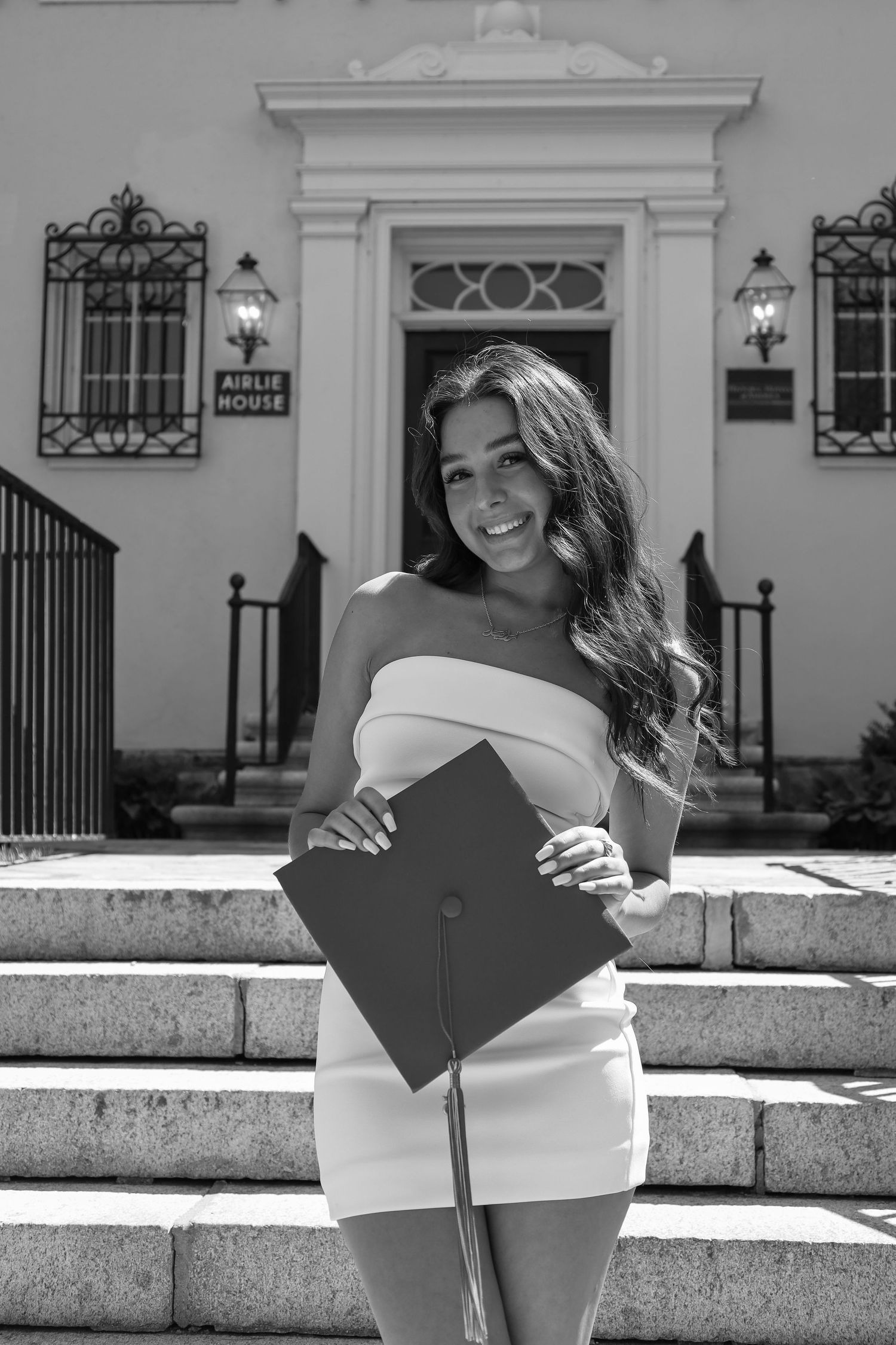 Graduate holding diploma poses in black and white on stone steps of an elegant building.