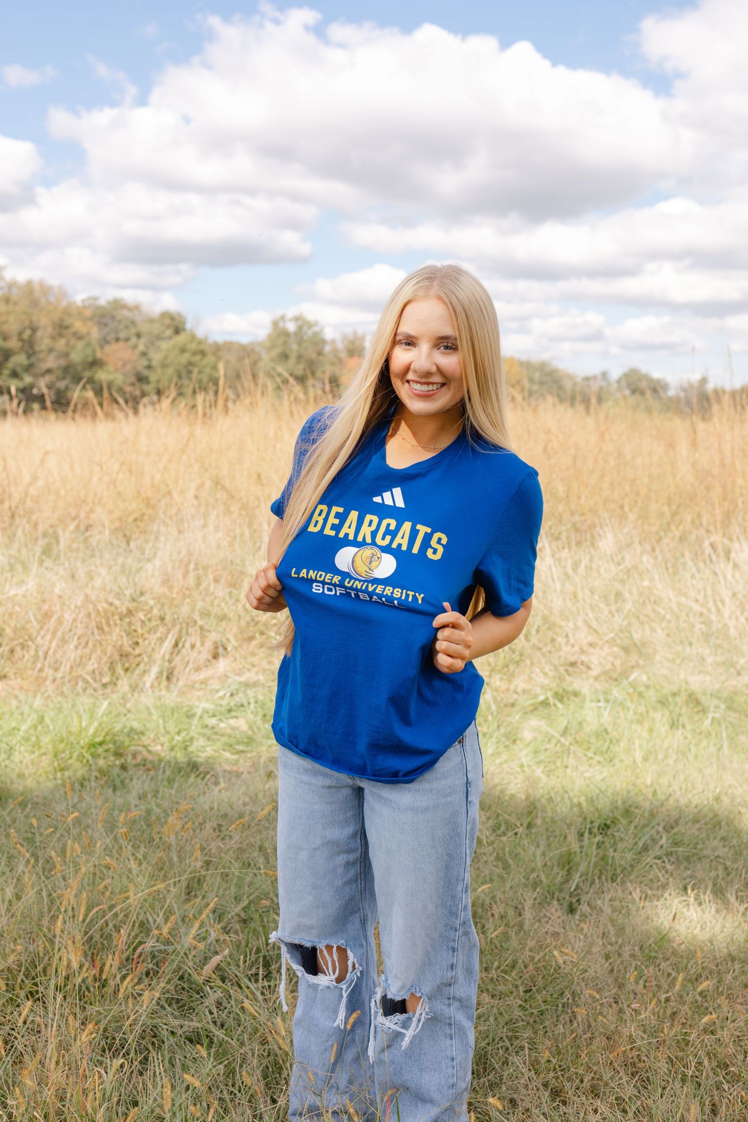 Young woman wearing a blue Bearcats Lander University t-shirt and ripped jeans standing in a golden field.