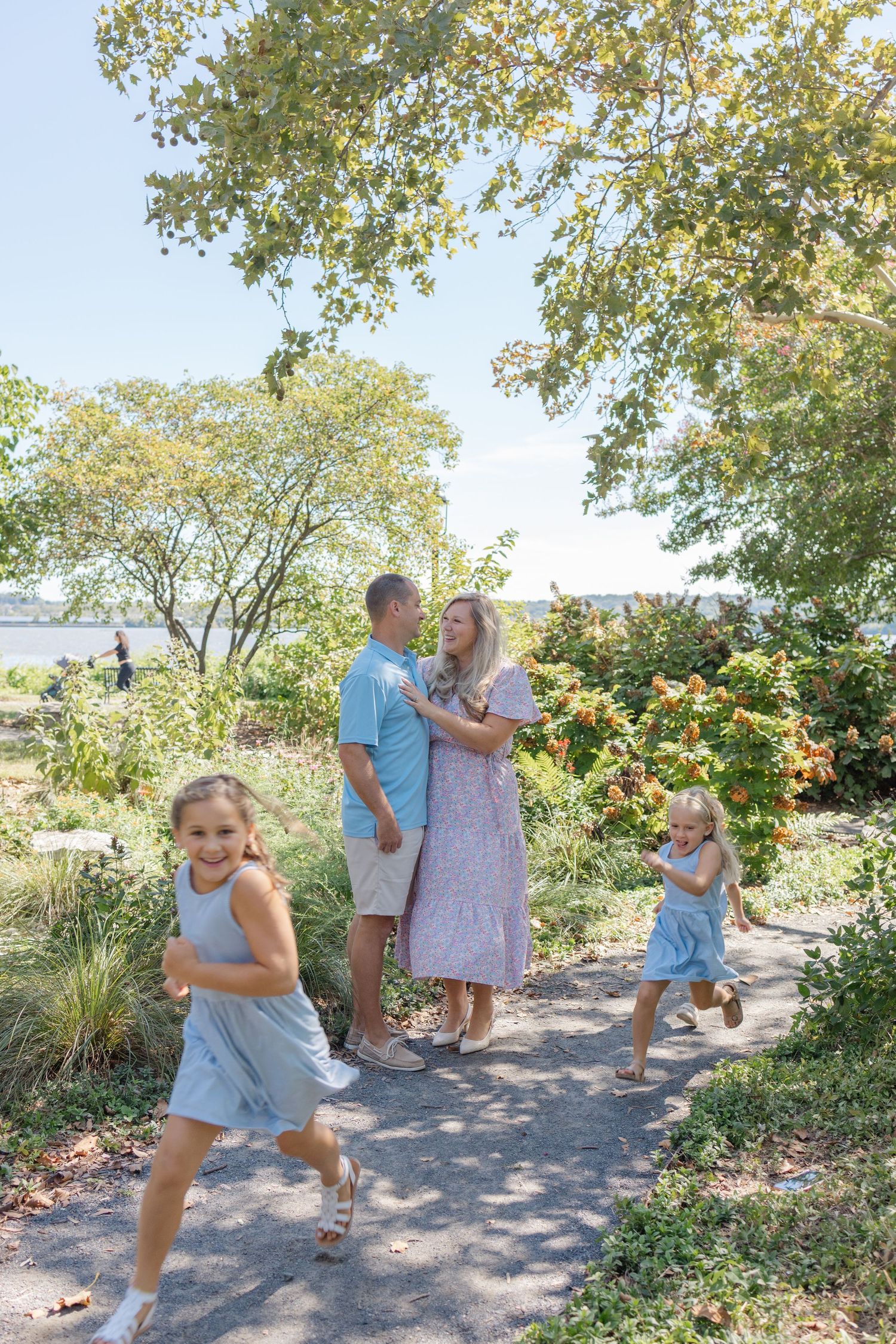 Family enjoying a playful moment together on a garden path surrounded by lush greenery and trees on a sunny day.