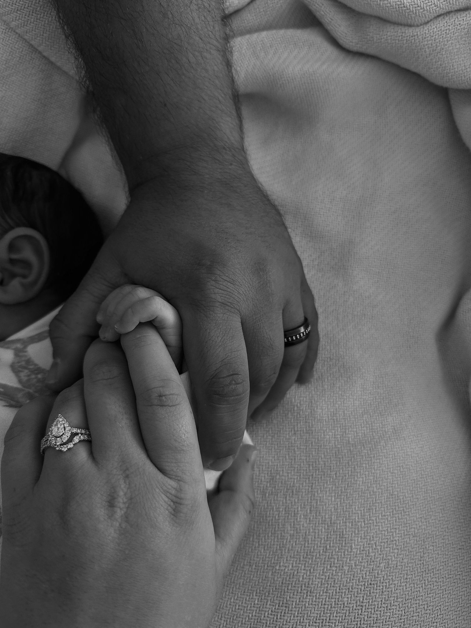 Black and white image of two hands clasped together with wedding rings visible.