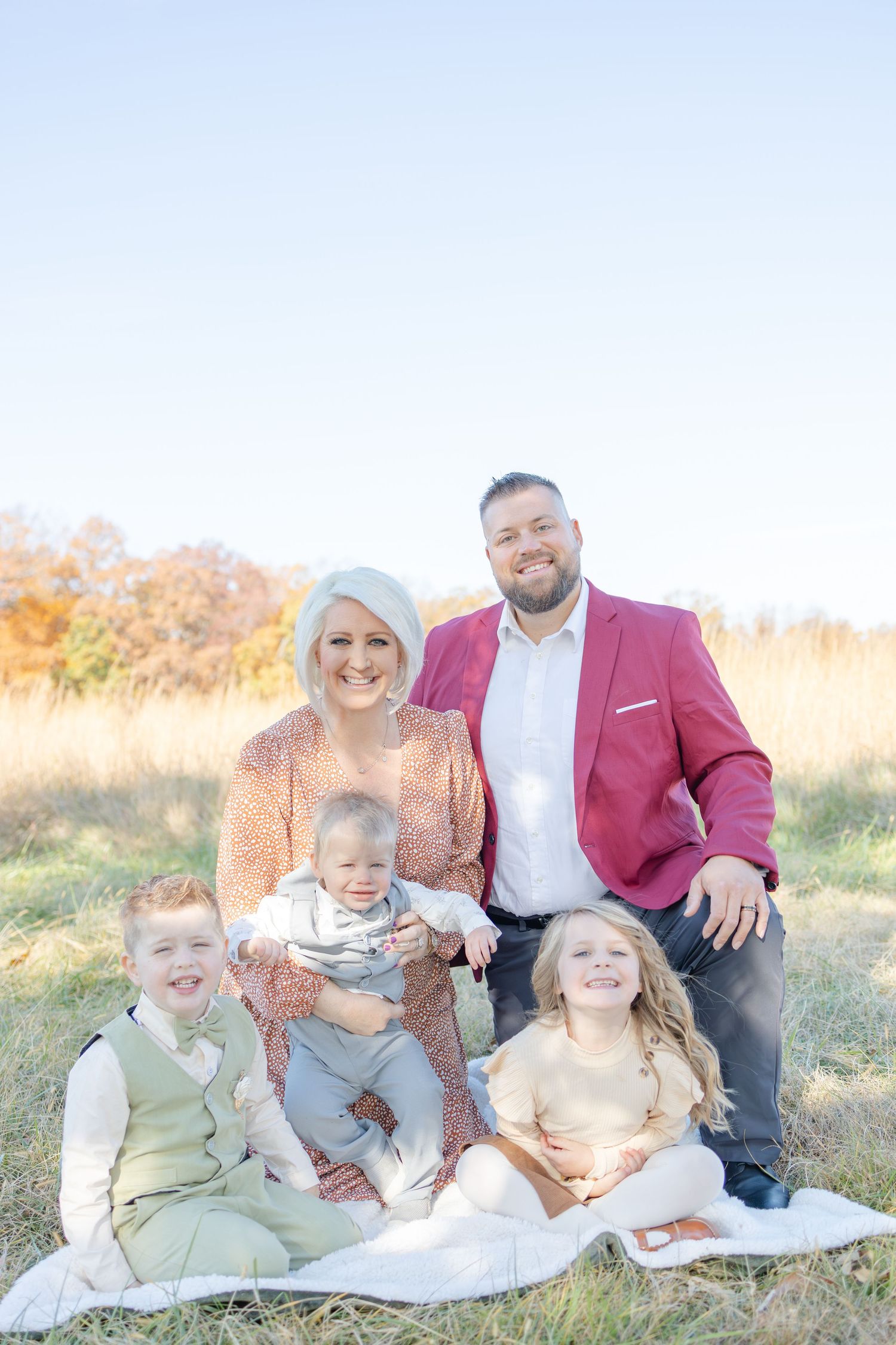 Family of five posing outdoors on a blanket in a field during autumn, smiling for a portrait photo.