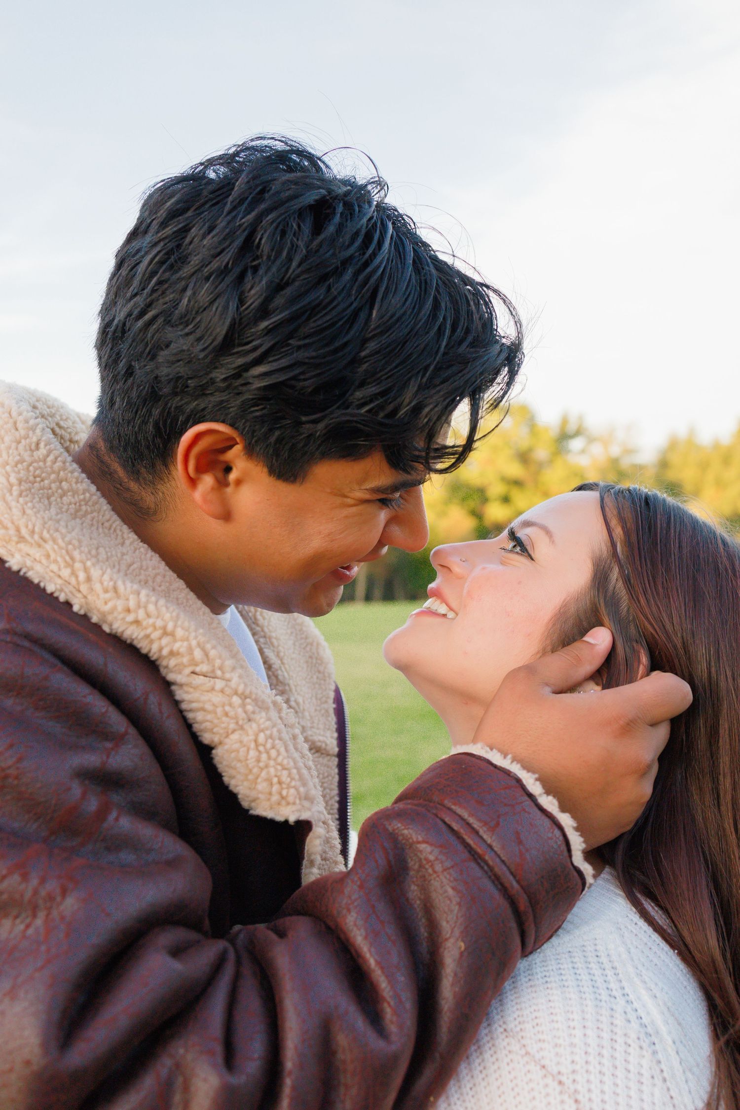 A young couple shares a romantic moment outdoors, with the man tenderly holding the woman's face as they lean in close.