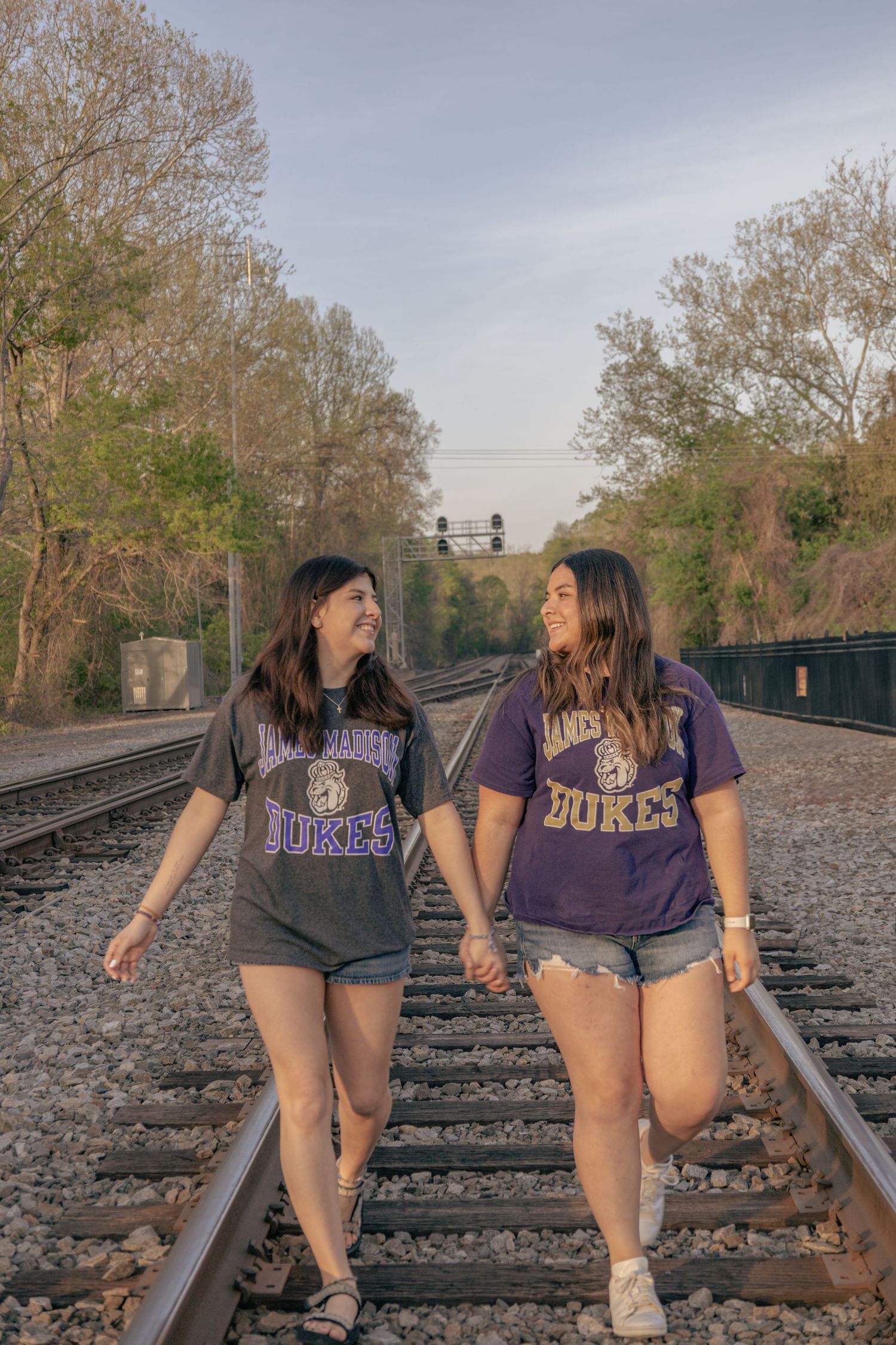 Two friends in Dukes t-shirts walk together on railroad tracks.