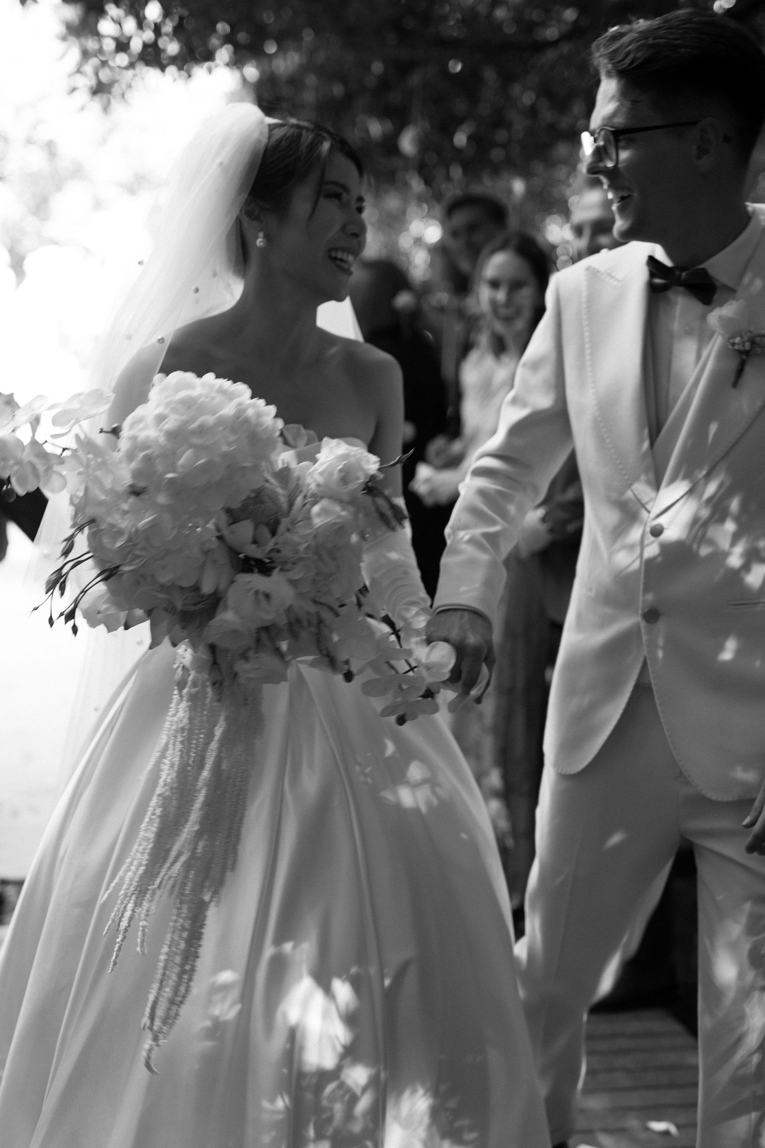 A romantic black and white photo of a wedding couple sharing a moment with a large white peony bouquet.