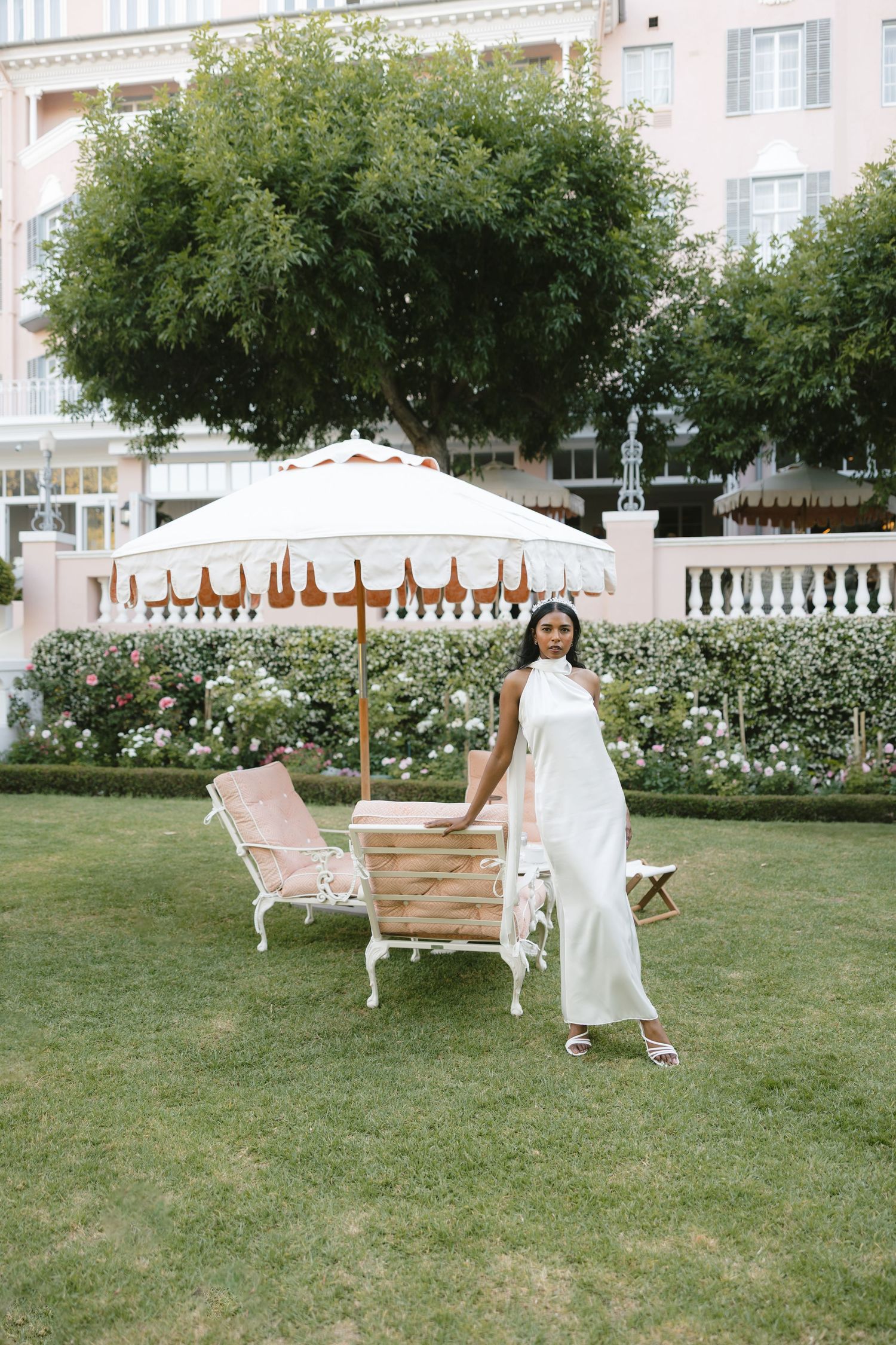 Elegant garden scene with white parasol, vintage chairs and pink building backdrop.