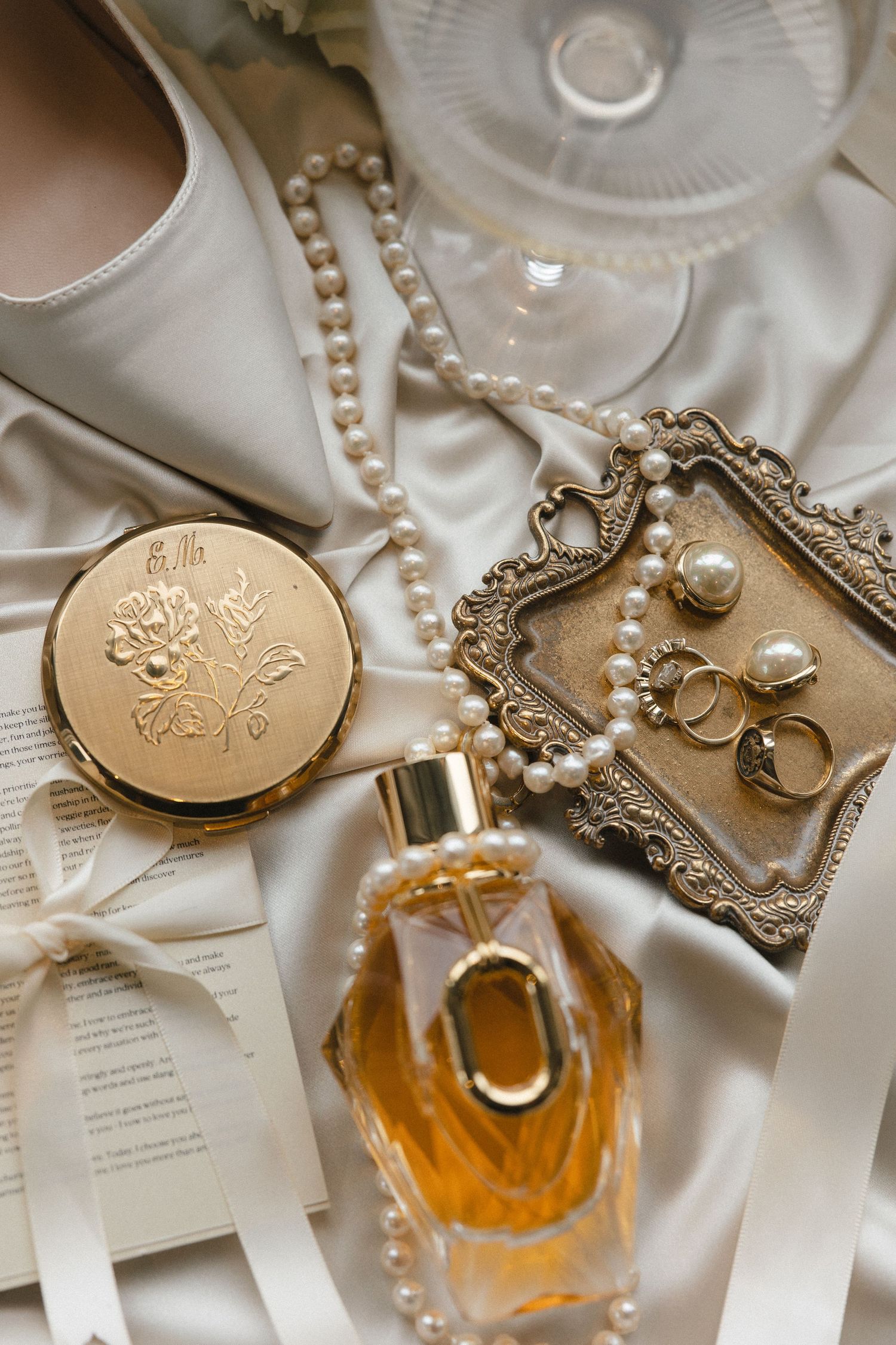 Vintage accessories including perfume, compact mirror and pearl jewelry on white silk.