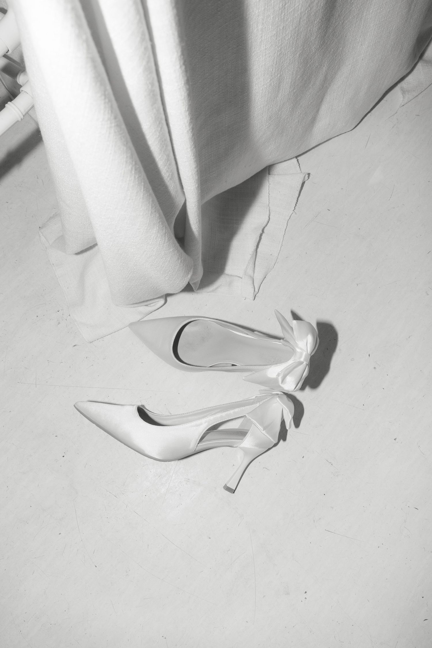 A pair of elegant white bridal heels photographed on a light floor in black and white.