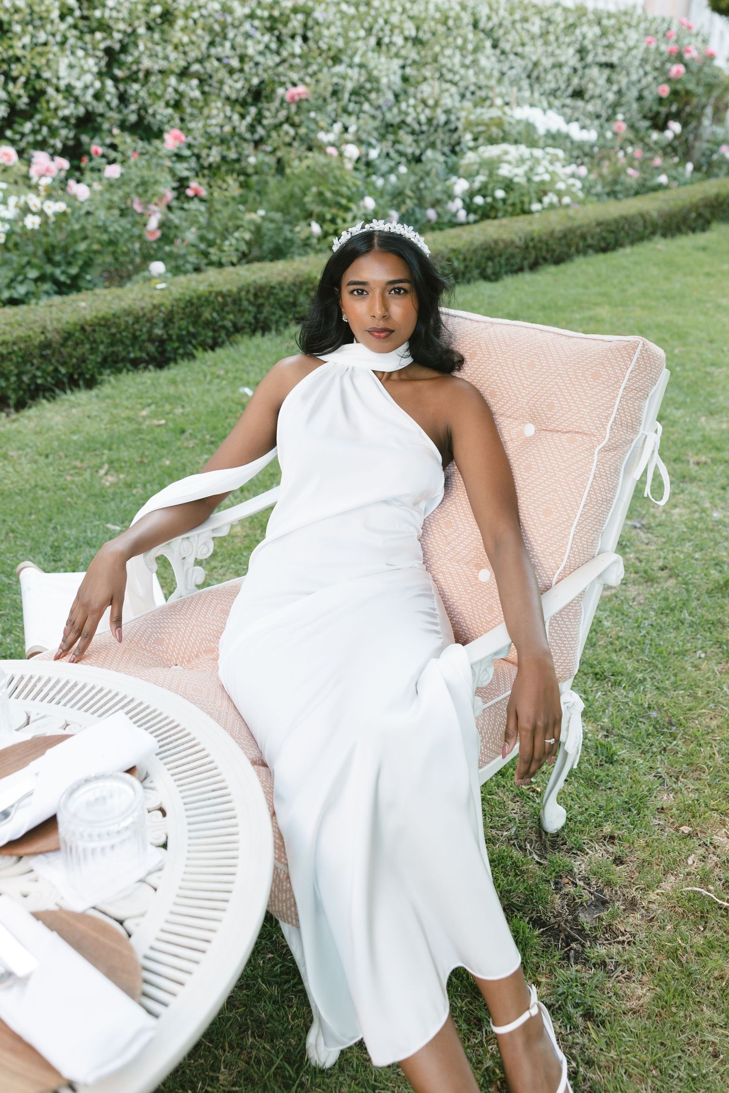Garden photoshoot featuring white halter dress and vintage blush lounge chair.