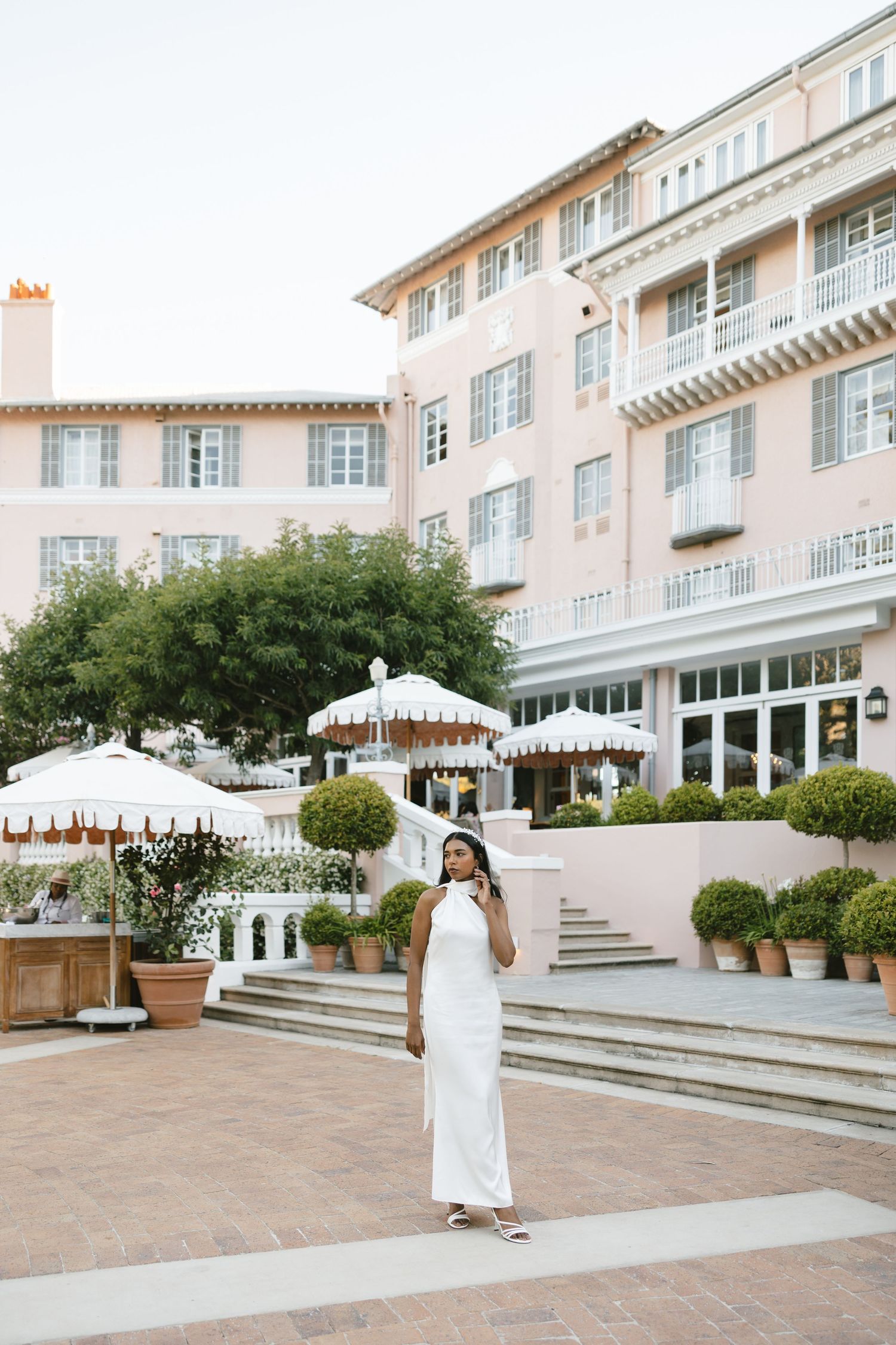 Luxury hotel exterior with pink facade, white umbrellas and manicured gardens.