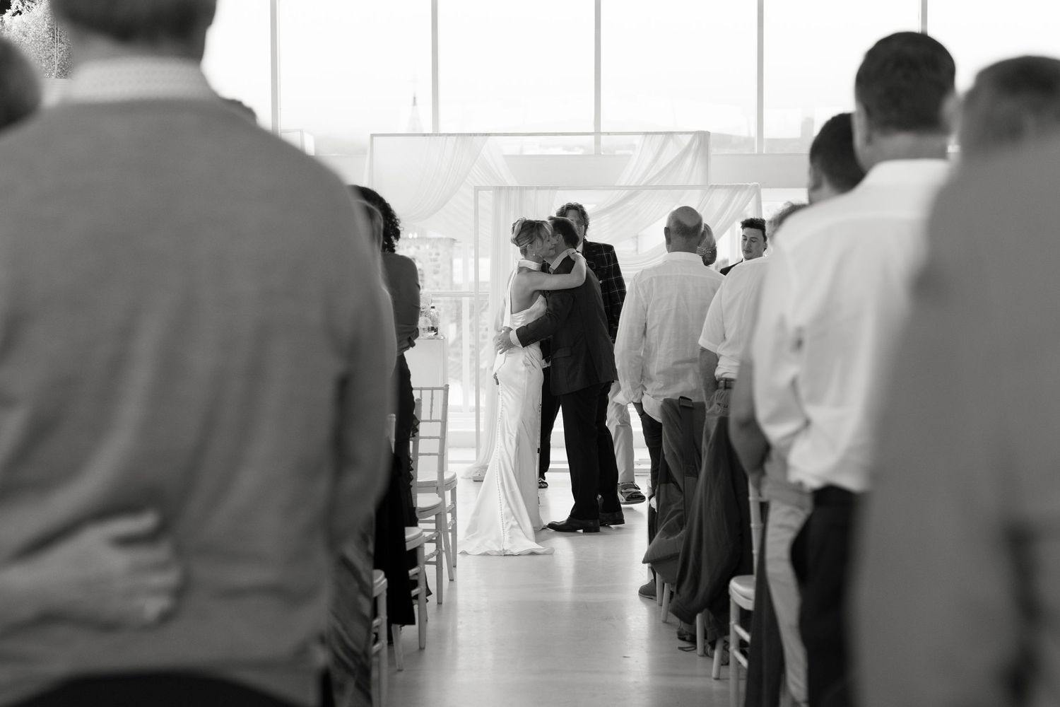 Black and white photo of wedding ceremony with guests watching couple at altar.