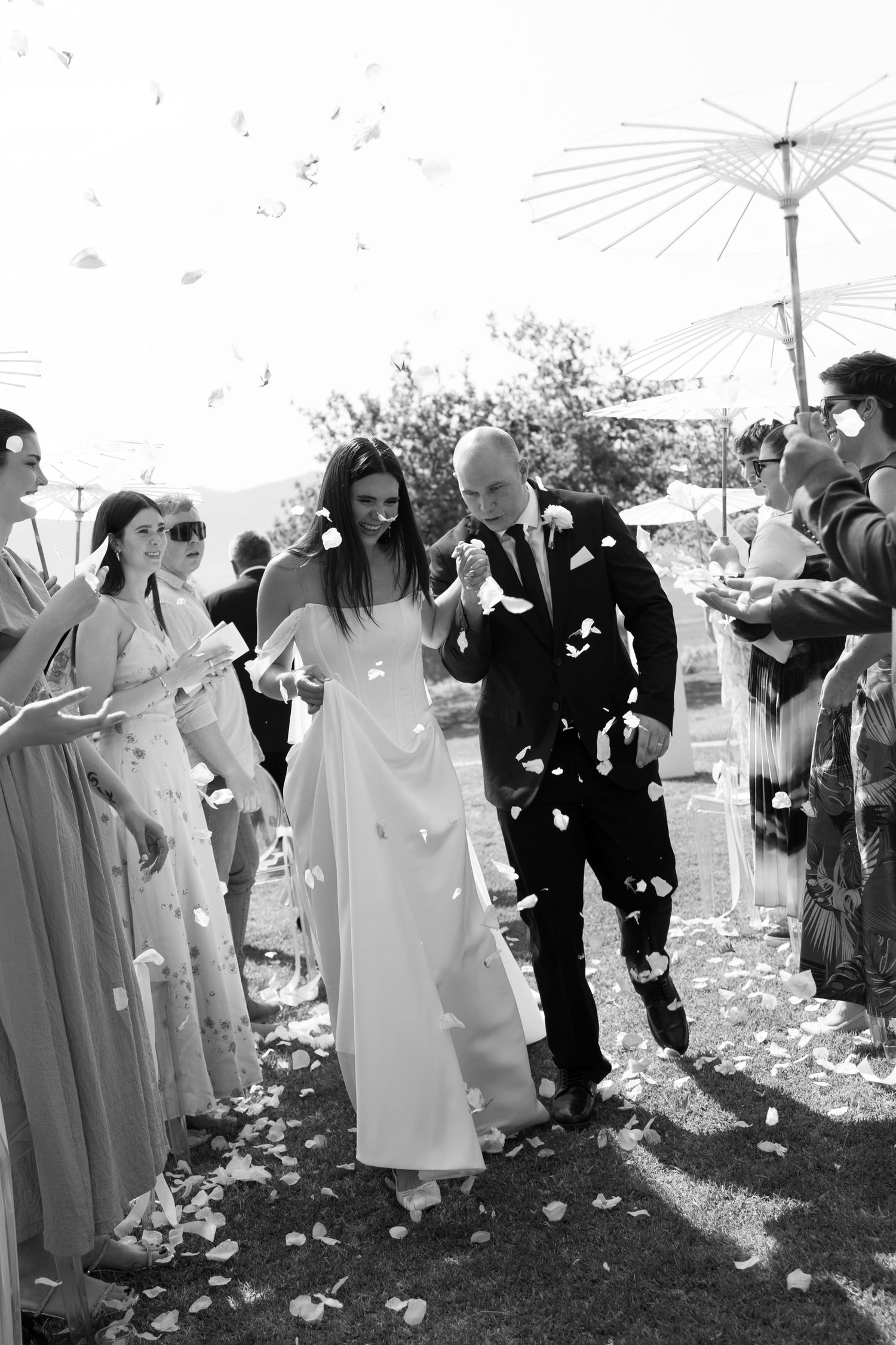 A festive wedding recessional with guests throwing flower petals as the newlyweds walk down the aisle.