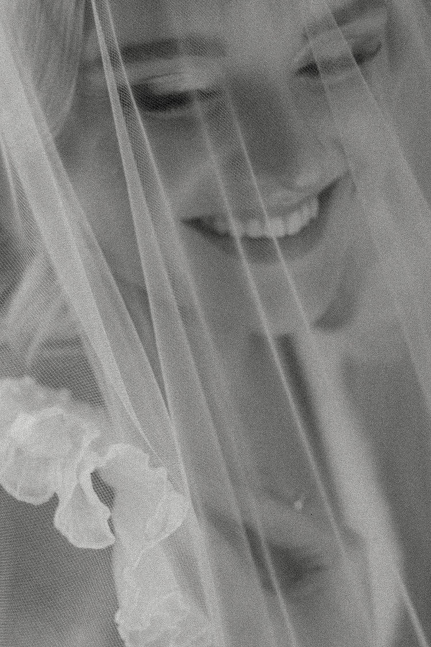 Artistic black and white close-up of a joyful smile behind a wedding veil.