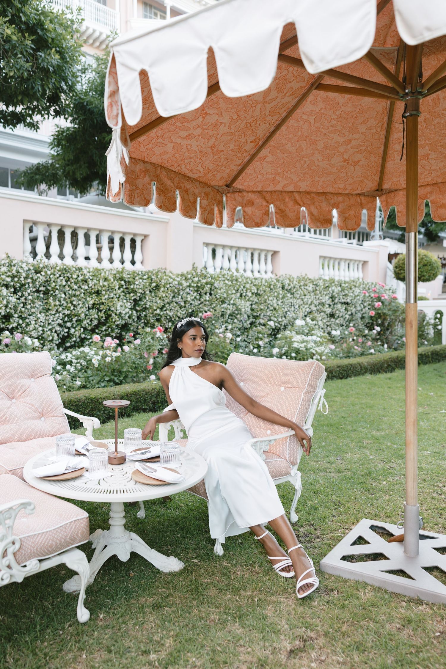 Outdoor tea setup under brown and white striped umbrella with pink chairs.