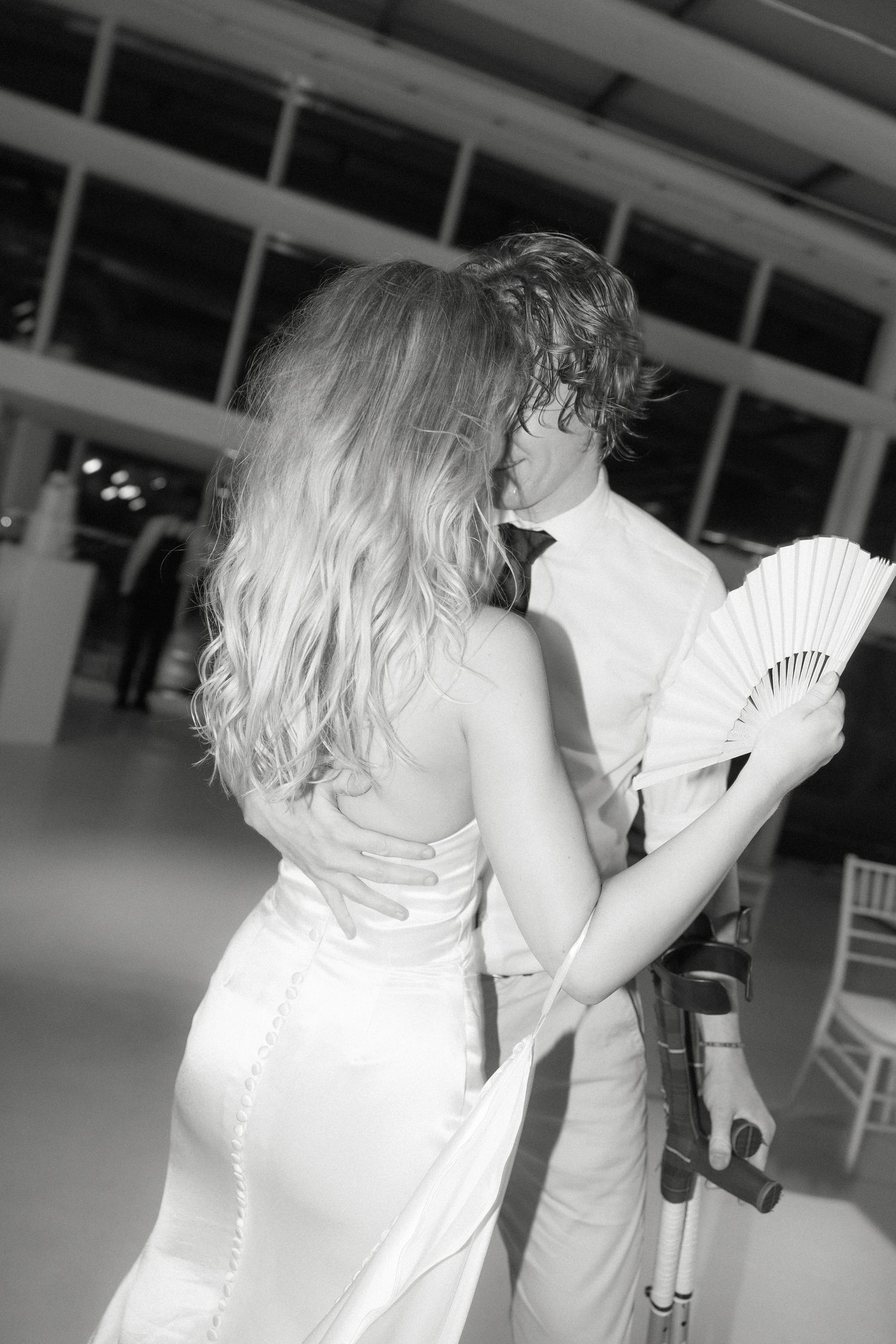 A black and white photo of a couple dancing, with the bride holding a decorative fan.