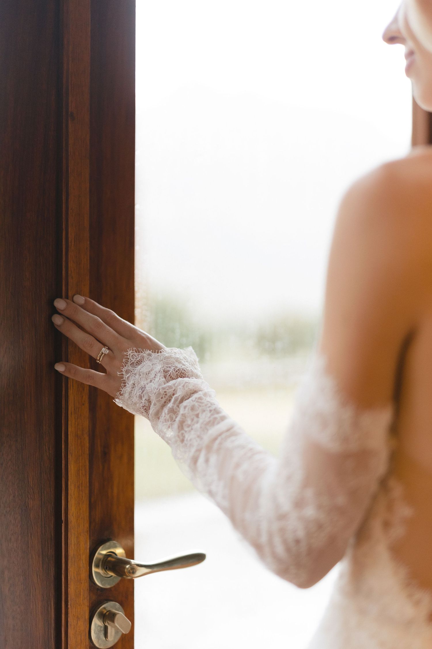 Delicate lace-gloved hand touching a wooden door handle in an elegant wedding dress sleeve.