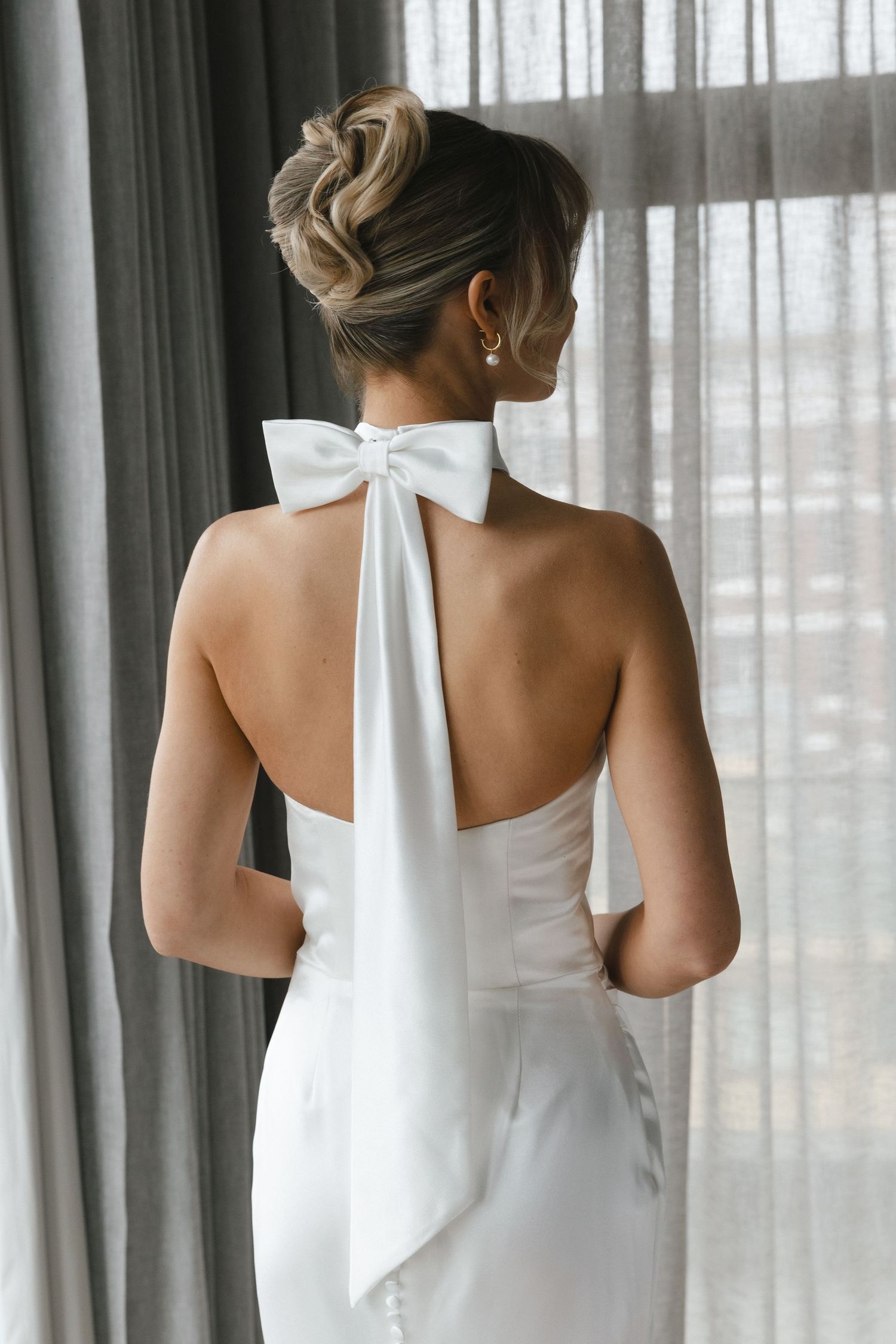 Elegant updo hairstyle and white bow detail on the back of a halter wedding dress.