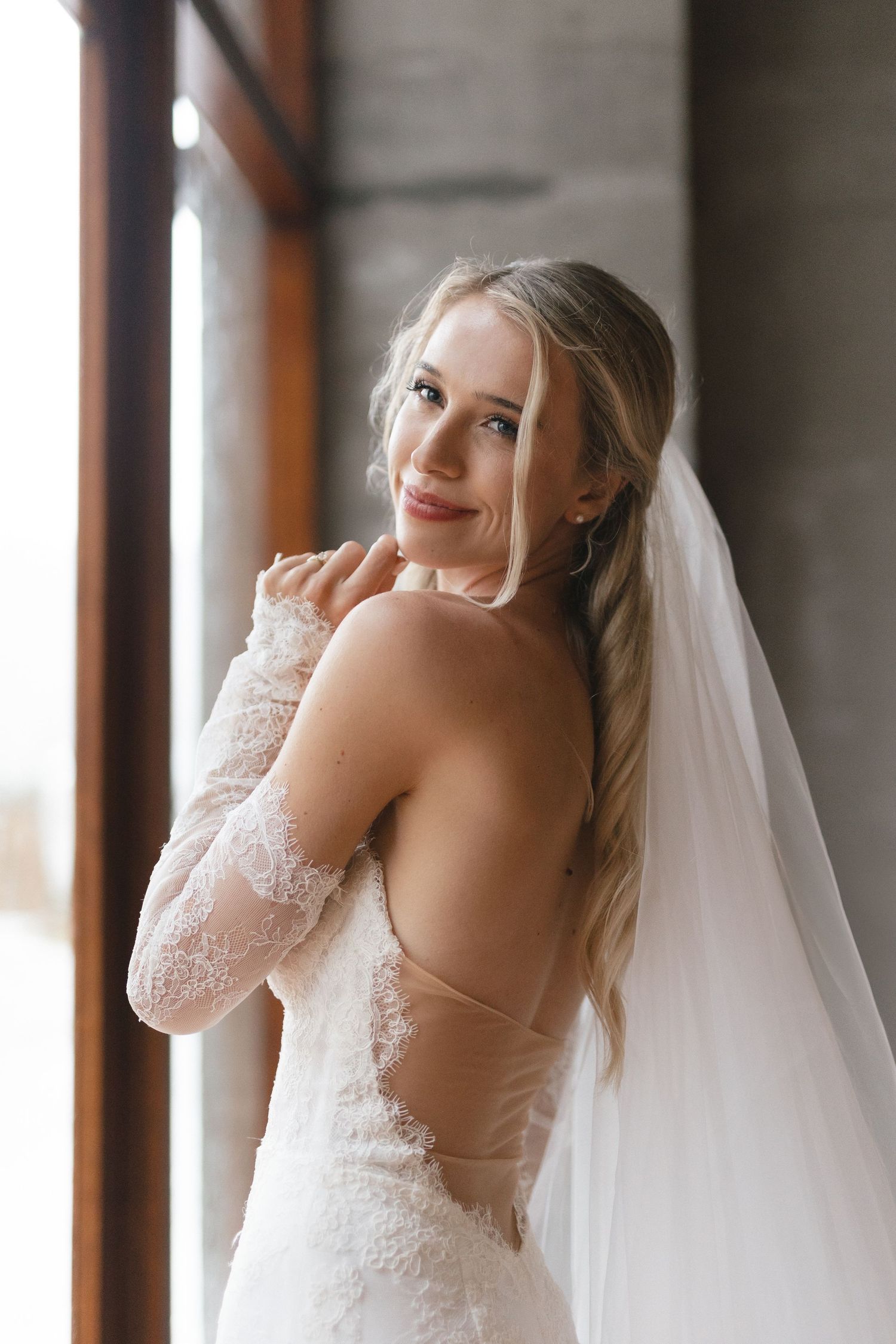 An elegant wedding dress with lace details and long veil captured in natural window light.