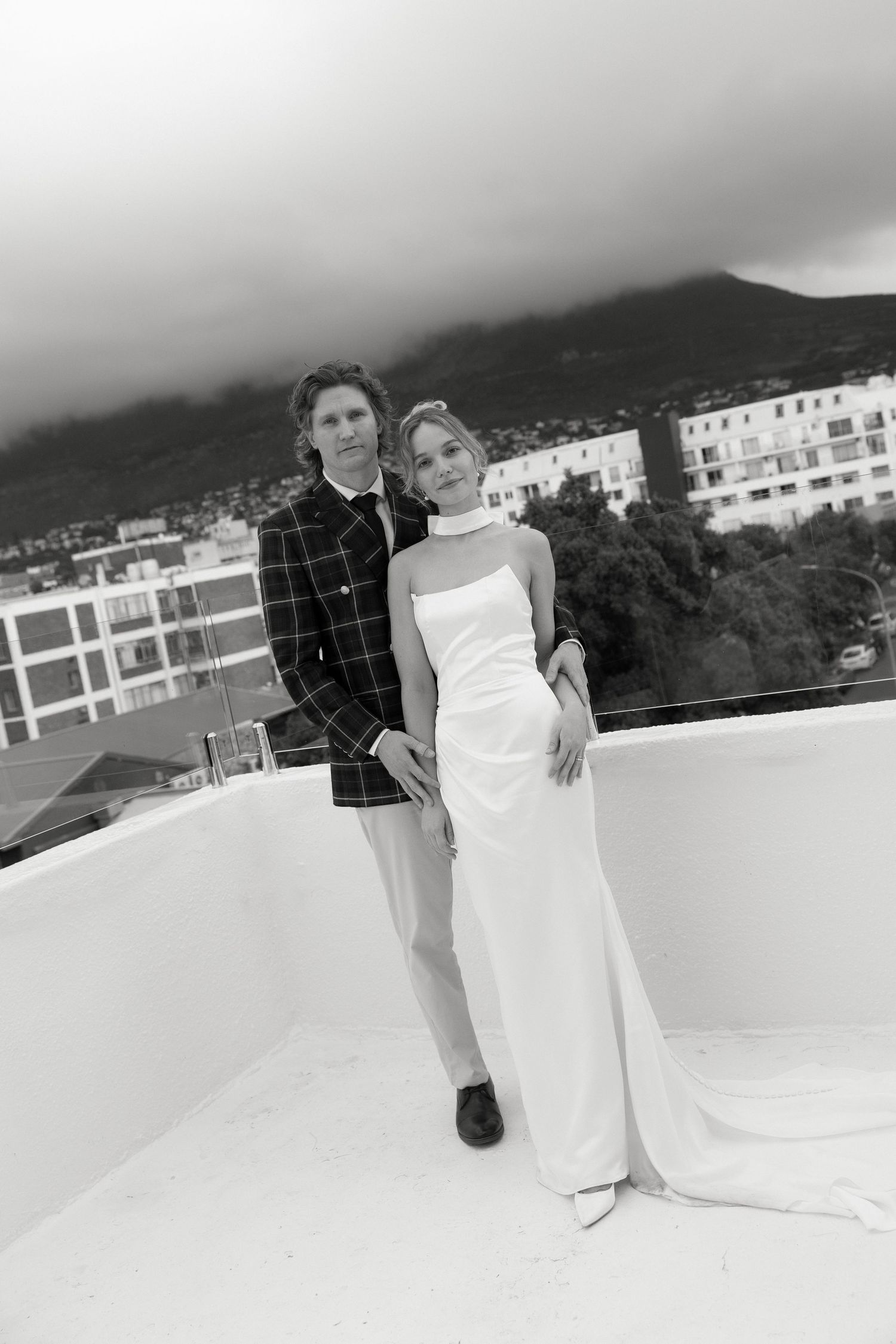 A black and white portrait of a couple on a rooftop with mountains in the background.