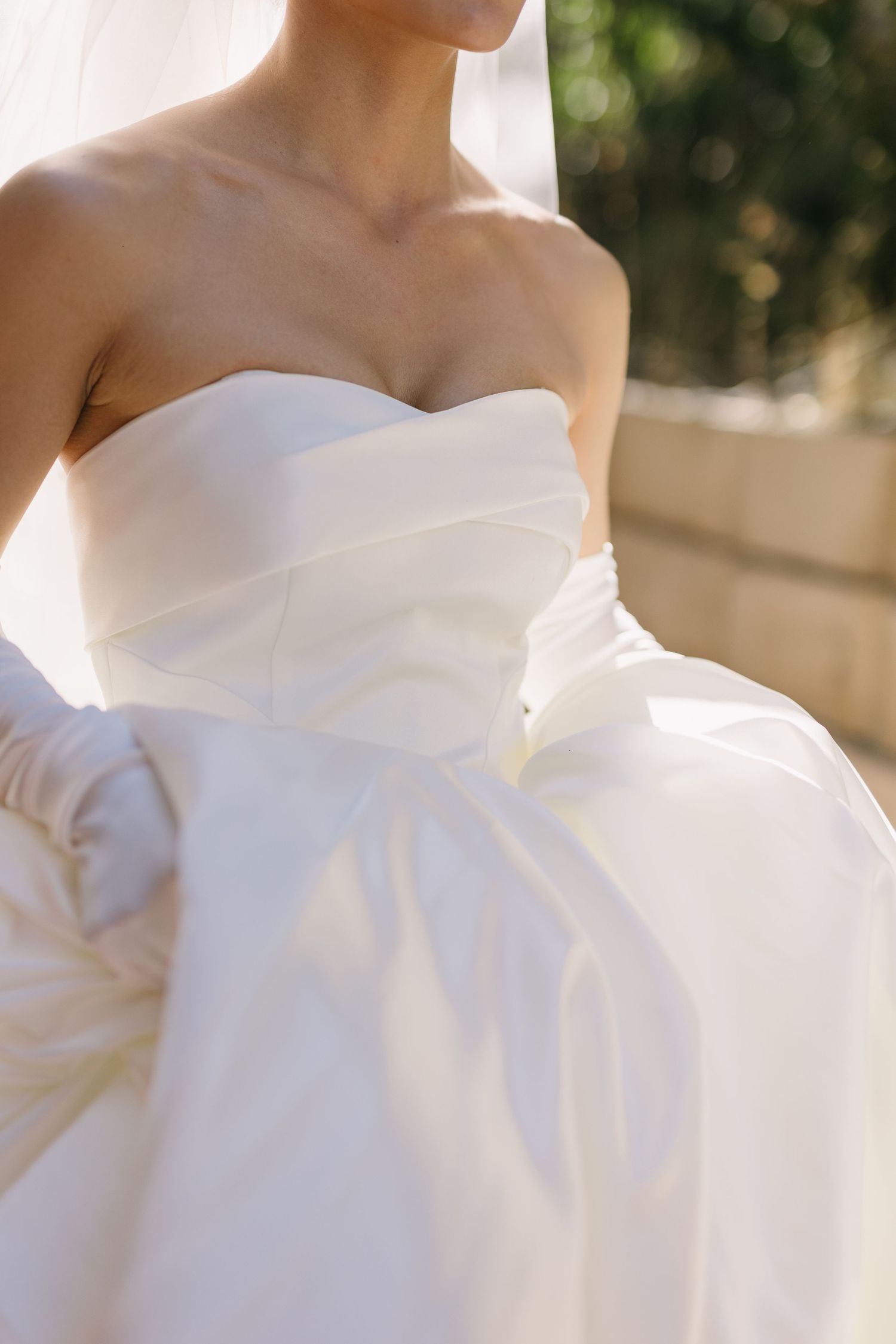 Close-up detail of strapless white wedding dress bodice in natural sunlight.