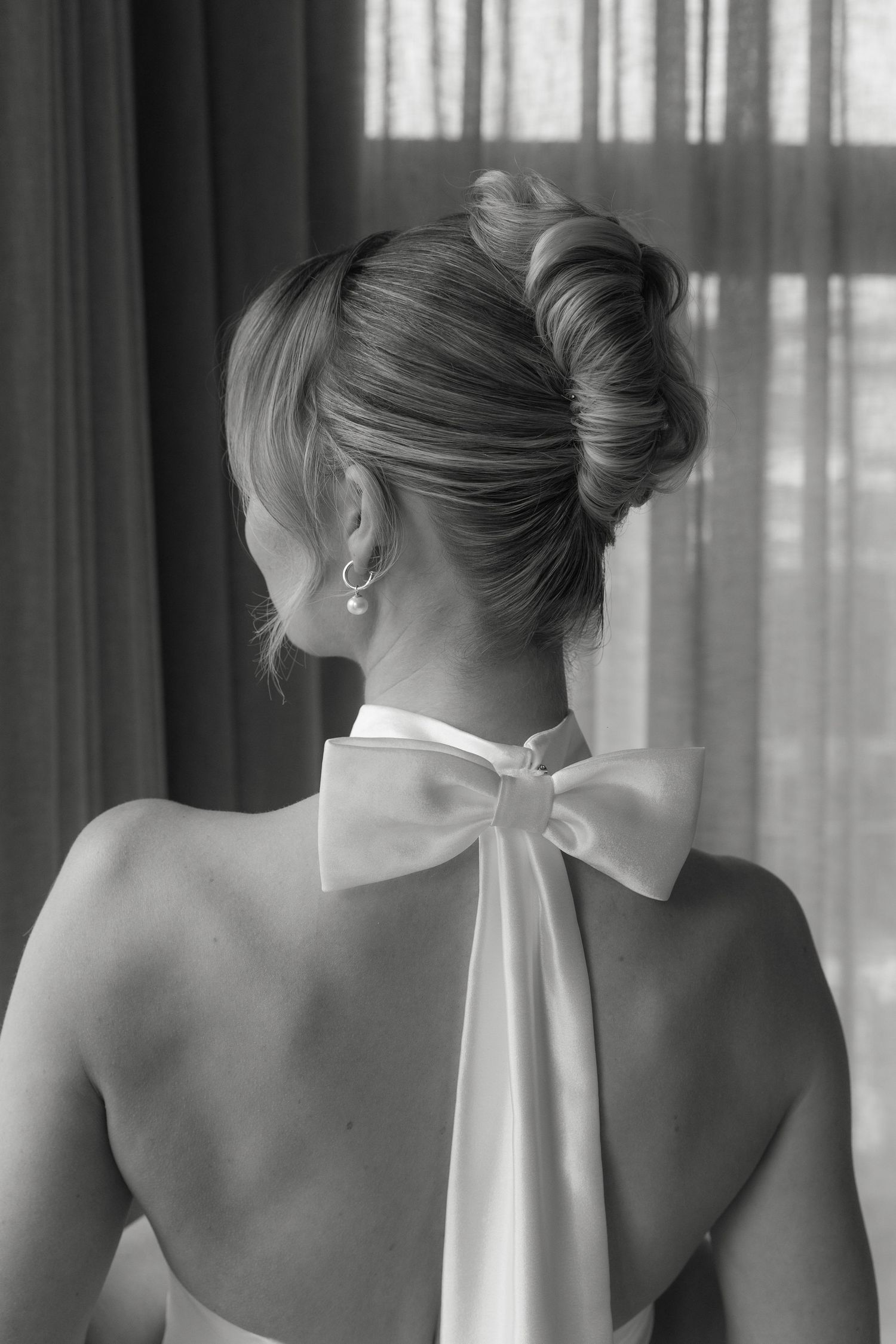 Black and white photo showing an elegant updo hairstyle and bow detail on halter neckline.