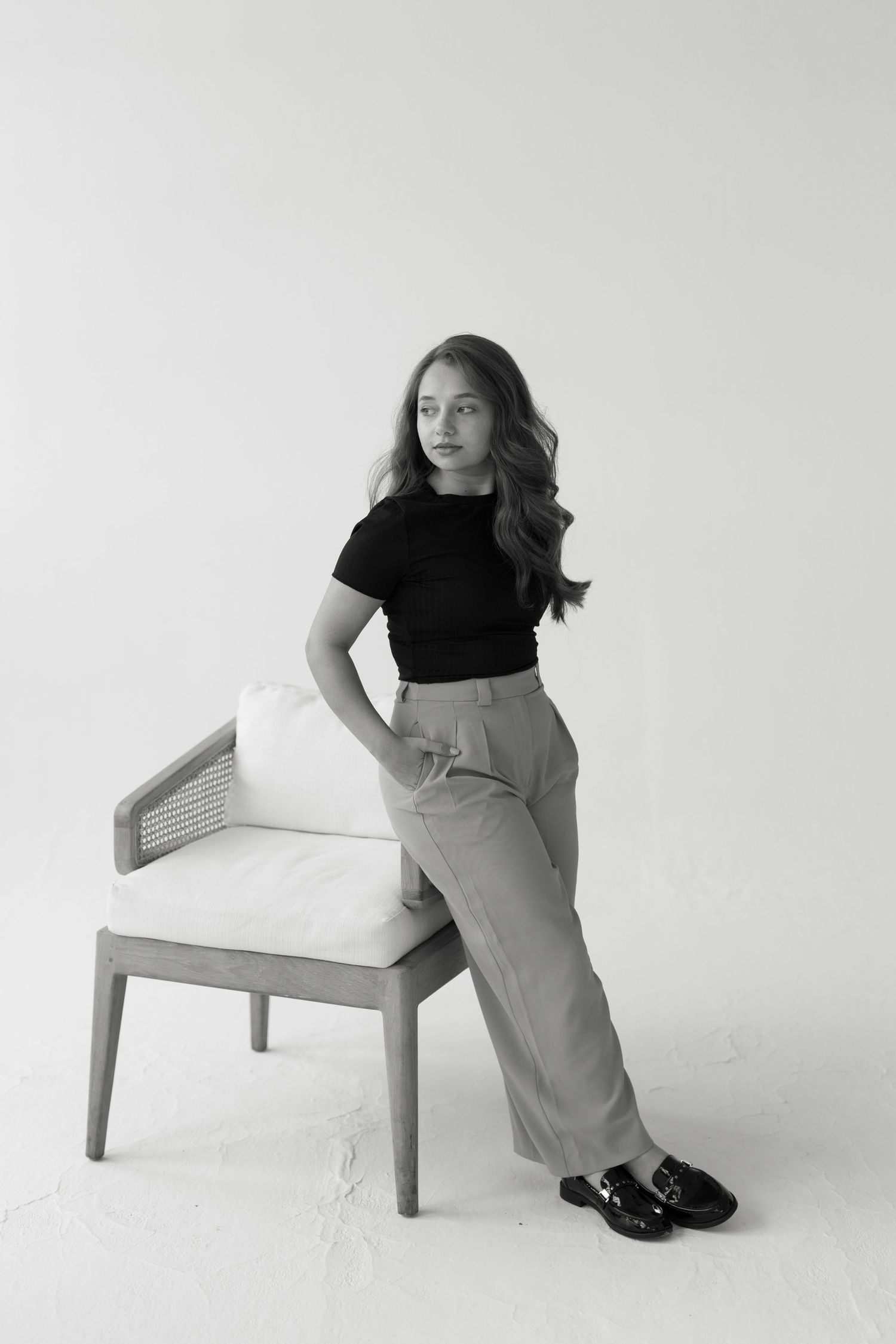 Stylish portrait featuring black top and grey trousers against minimalist background.