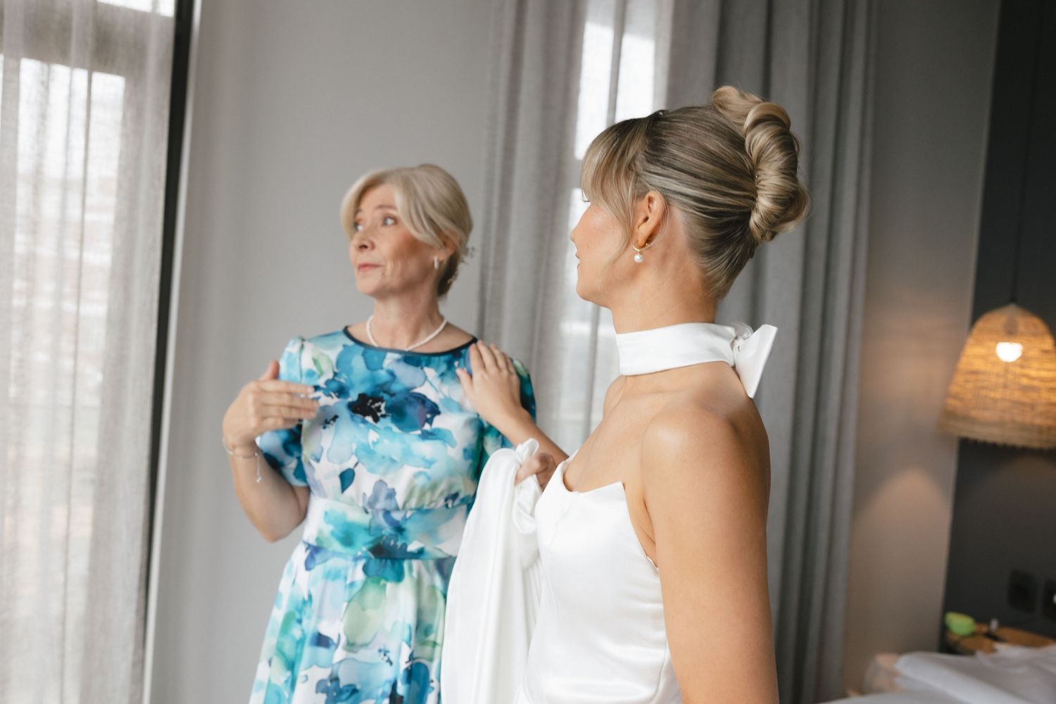 Two people share a tender moment while getting ready in a bright room, one wearing a blue floral dress.