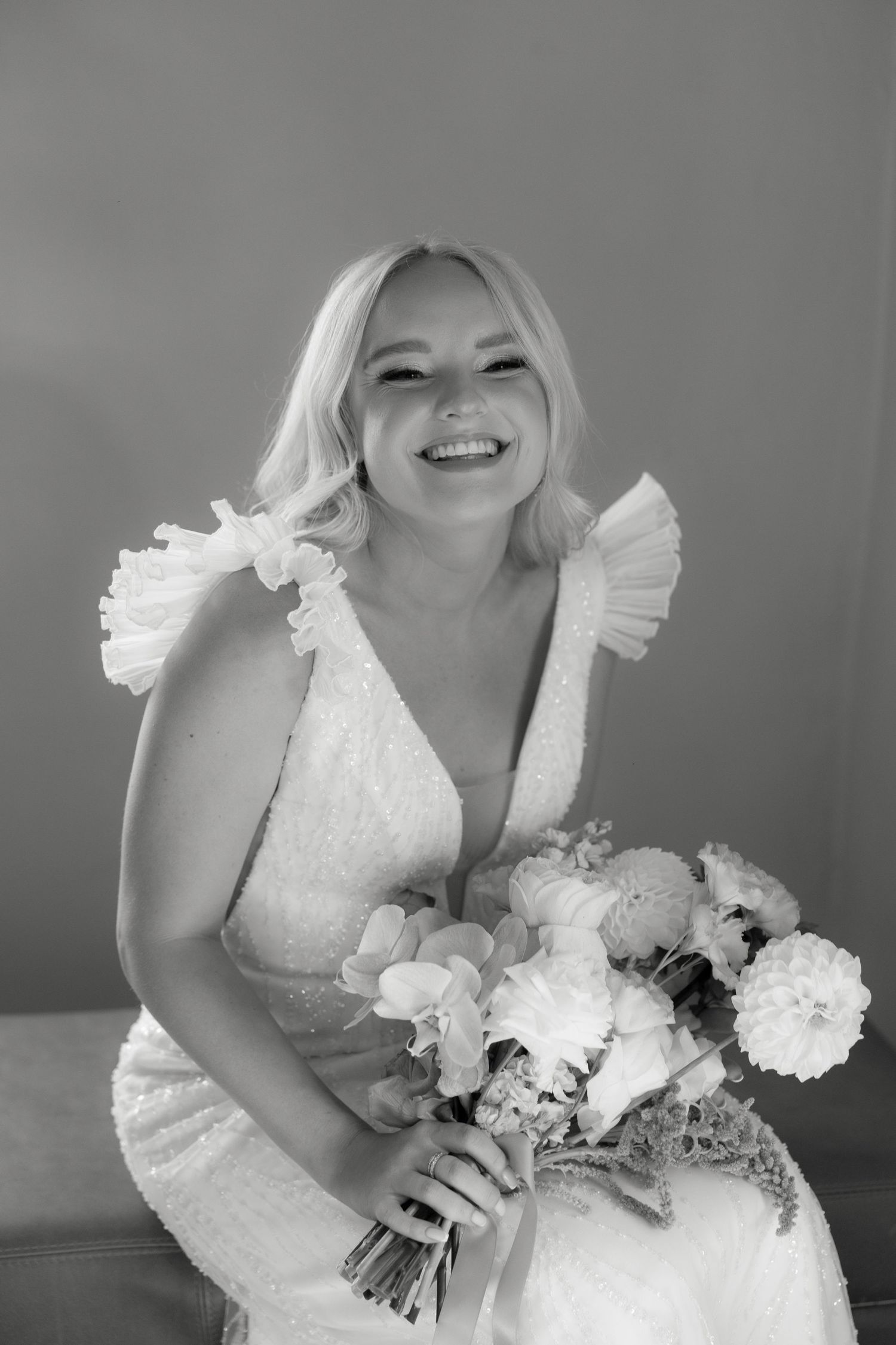Black and white portrait of a radiant bride in a ruffled wedding dress holding a bouquet.