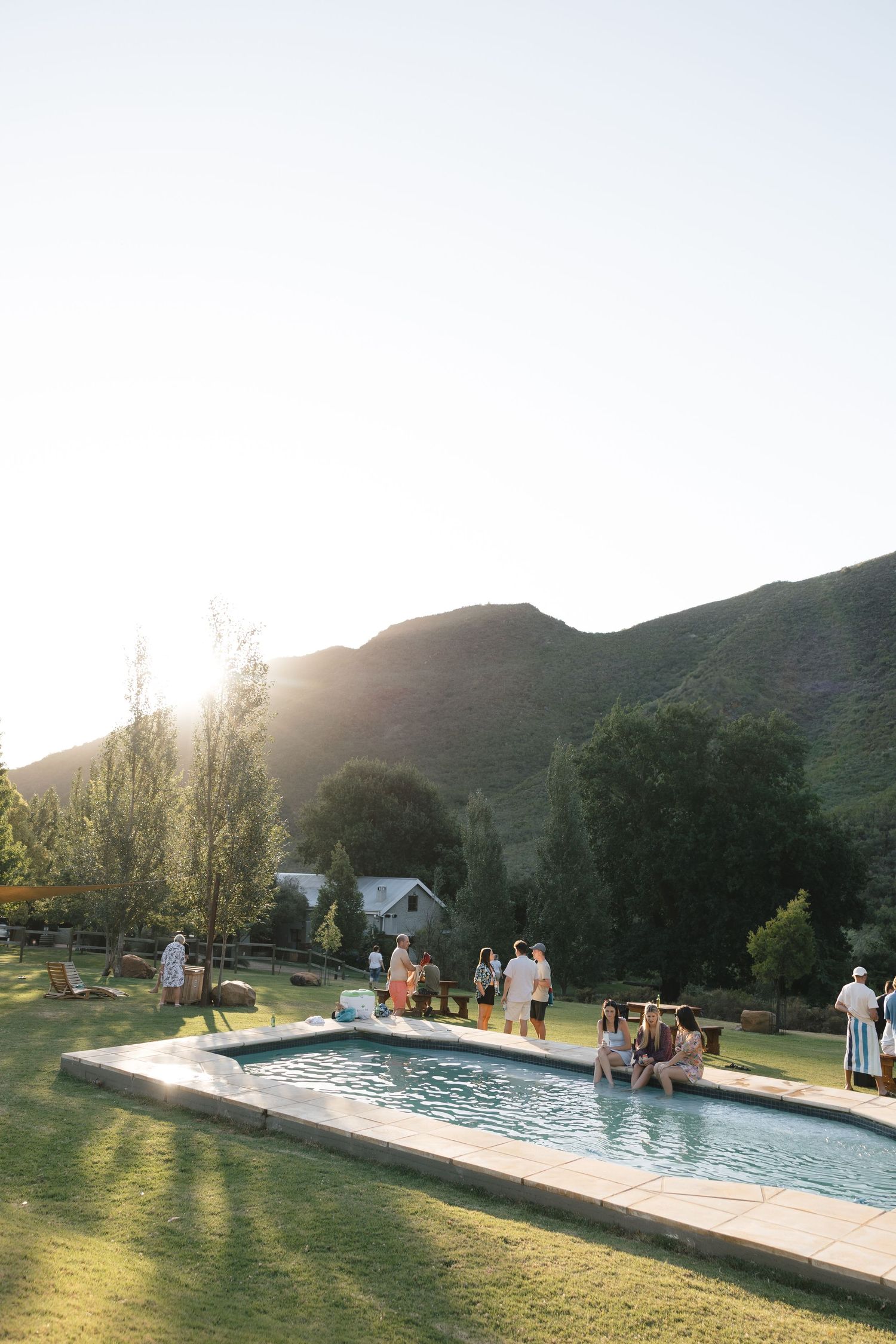 Wedding guests enjoying a poolside reception with mountains in the background at sunset.