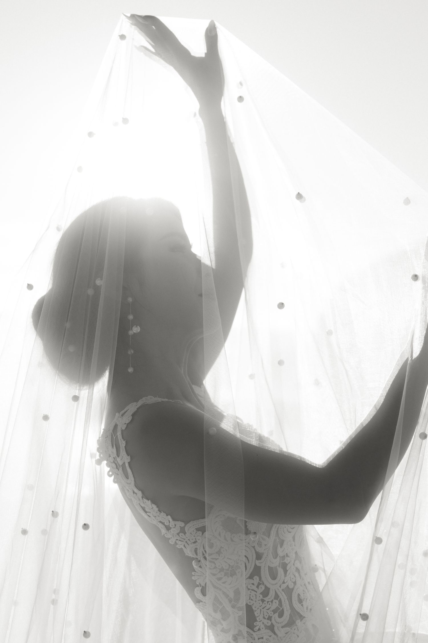Artistic silhouette of bride adjusting veil in ethereal backlit setting.