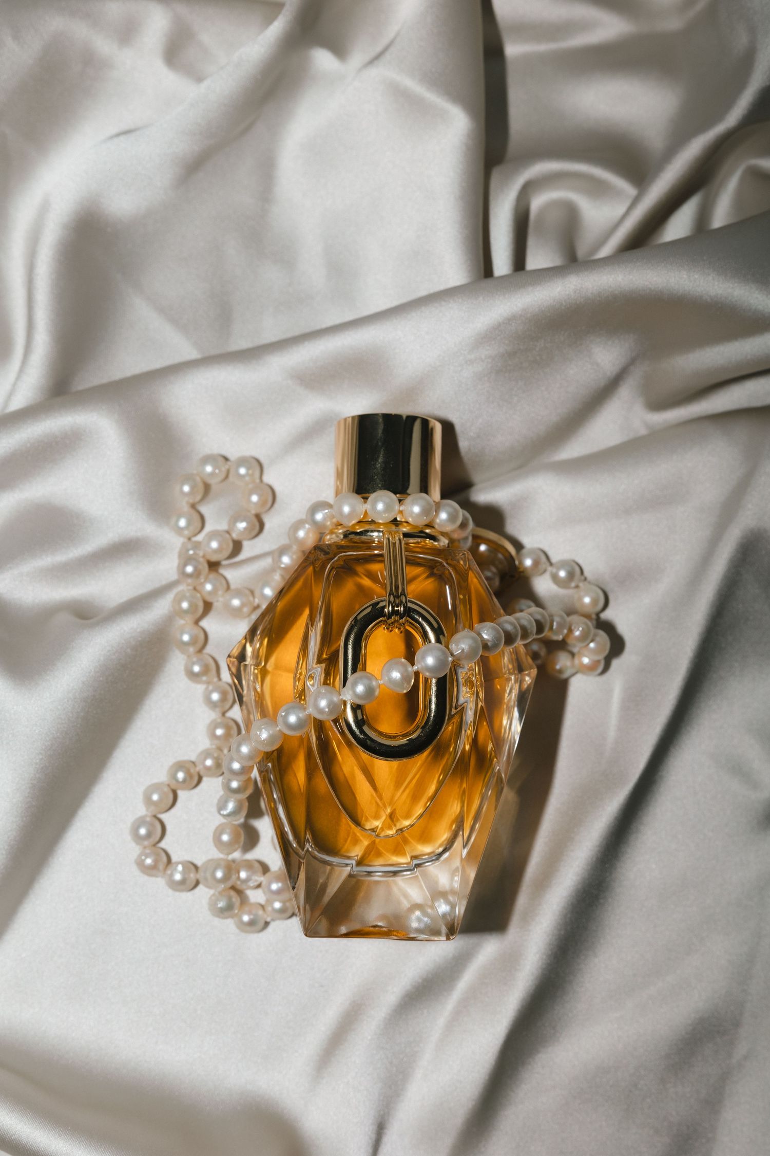 Perfume bottle with pearl necklace on white silk fabric.