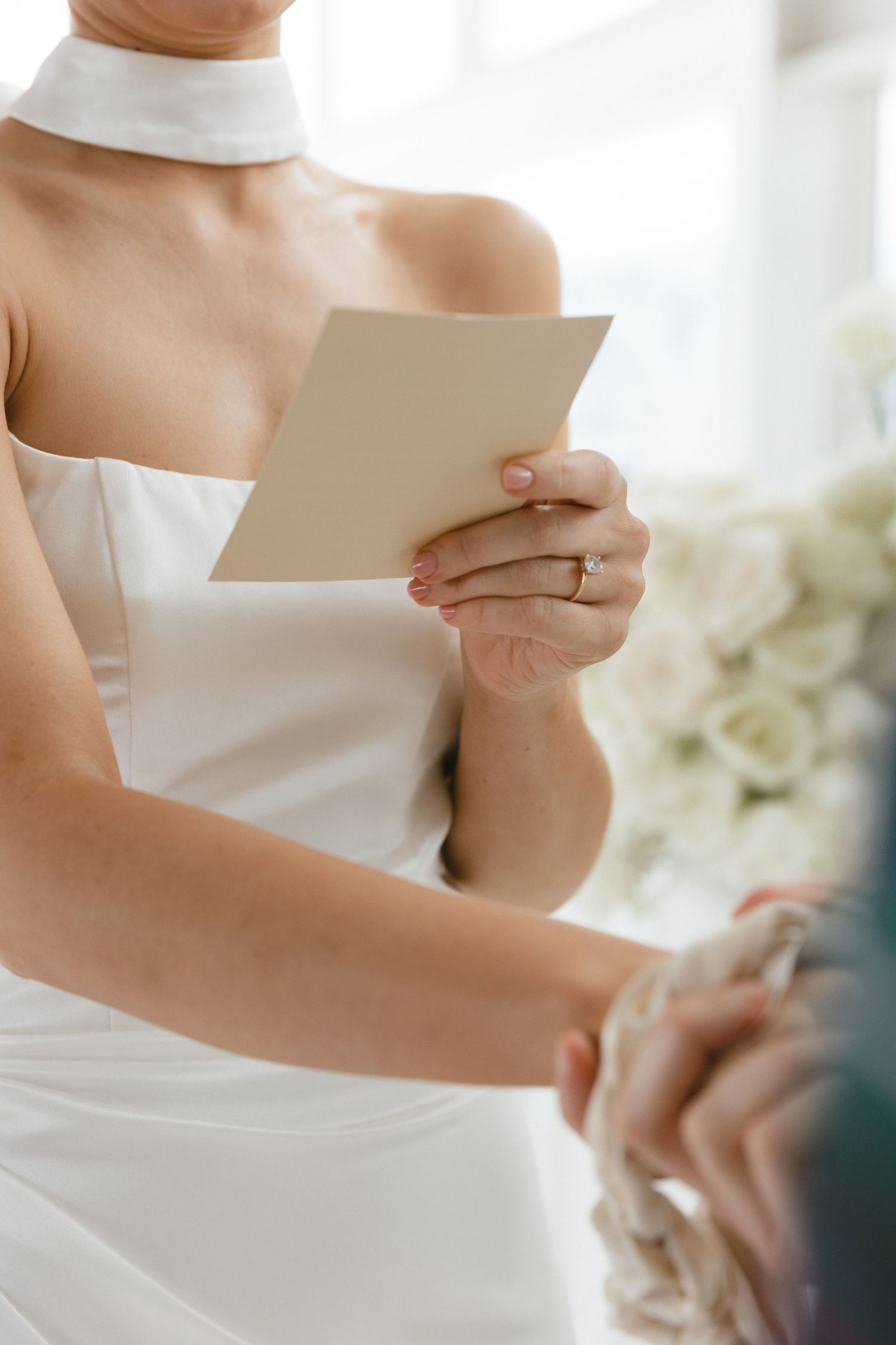Close-up of hands holding paper while wearing elegant white dress with high neckline.