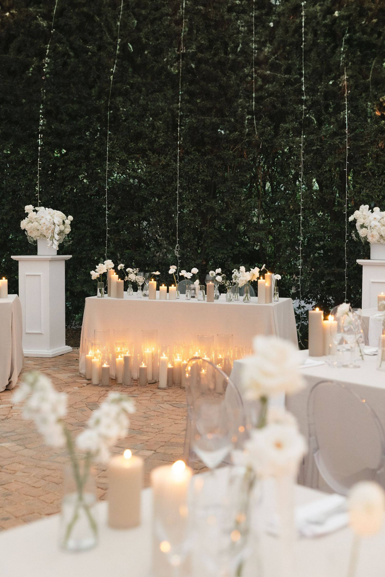 Elegant wedding reception table with glowing candles and white floral arrangements against a dark backdrop.