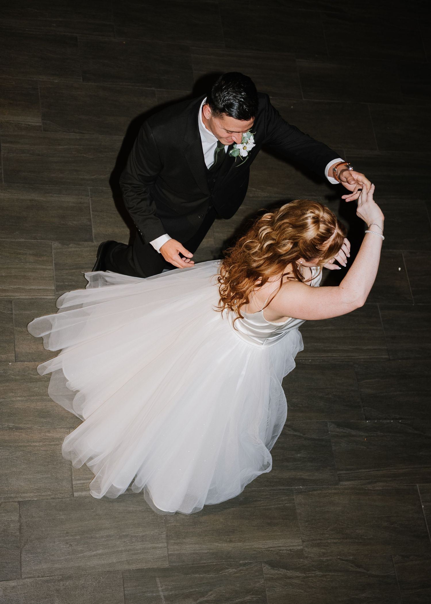 Aerial view of bride and groom sharing first dance, white tulle gown spinning on elegant wood floor.