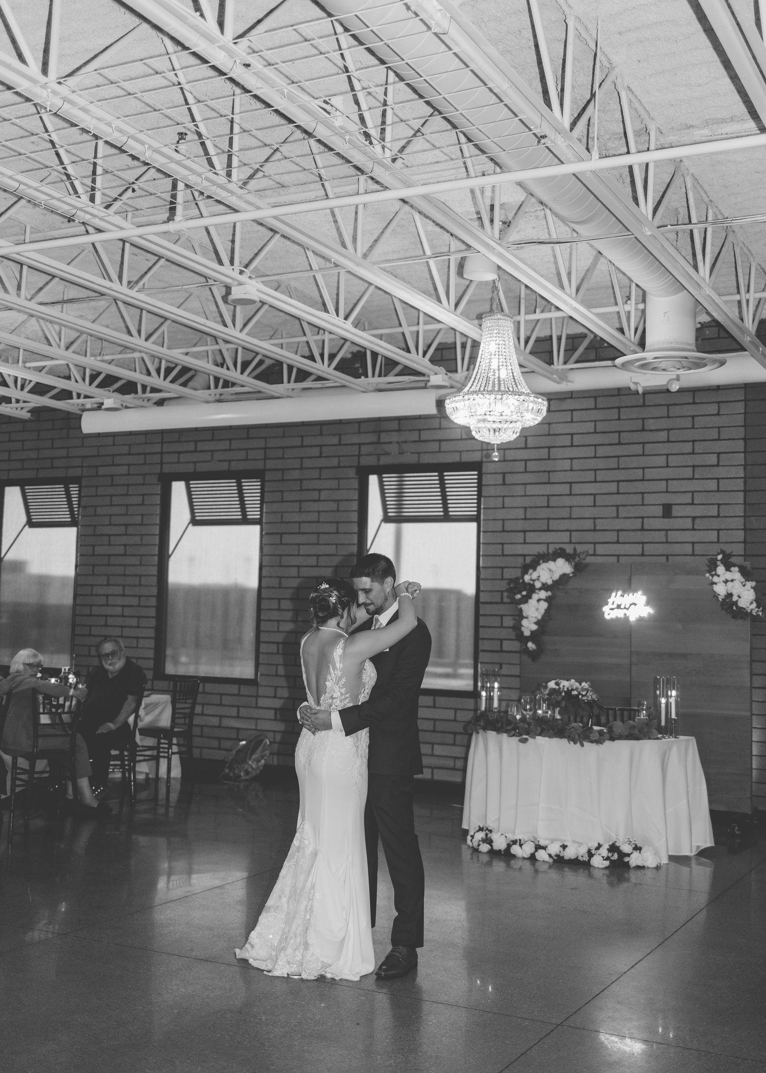 A couple shares a romantic first dance at their wedding reception in a brick-walled venue with exposed ceiling beams.