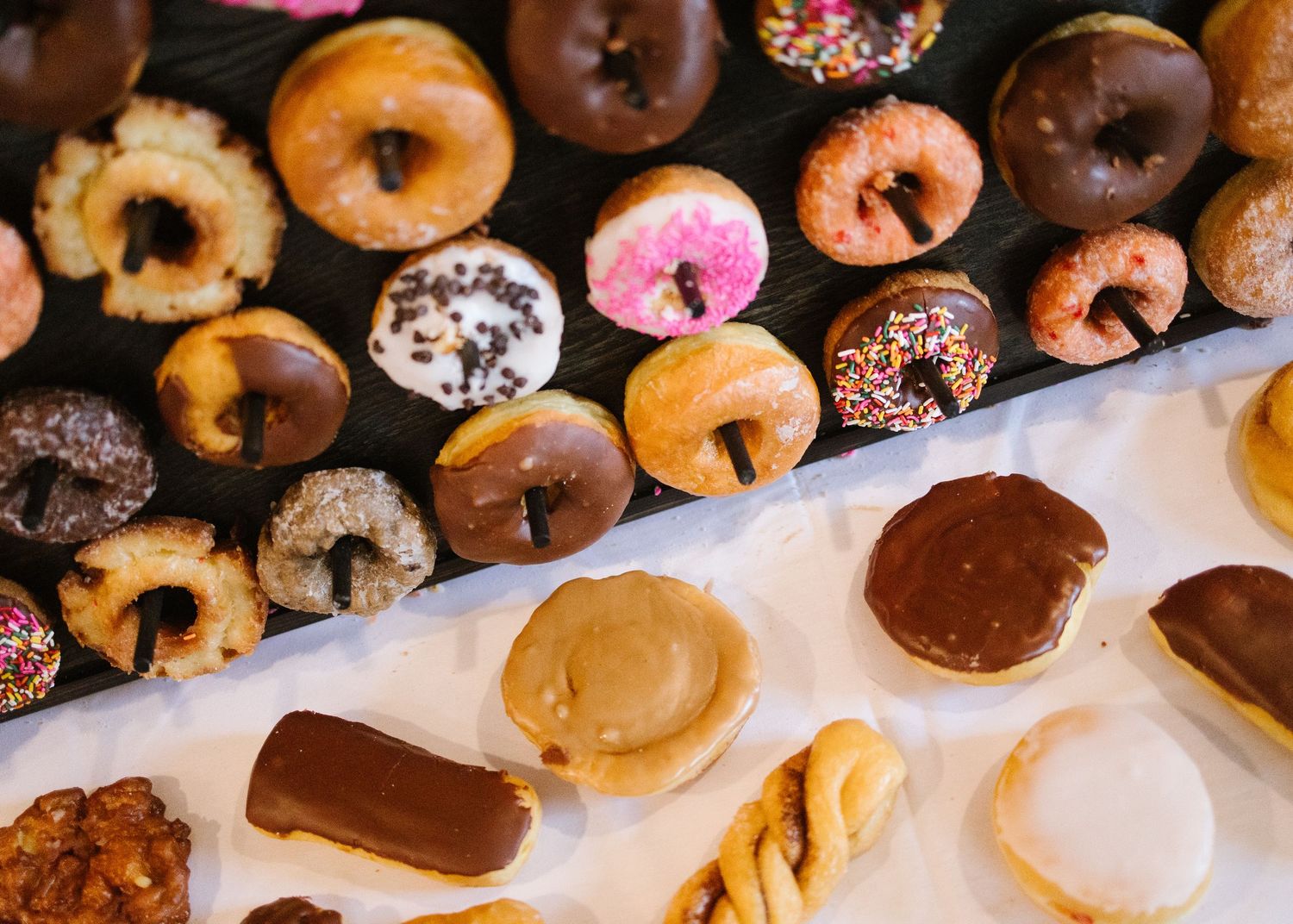 Assorted donuts with chocolate, glazed, and sprinkled toppings arranged on a white surface.